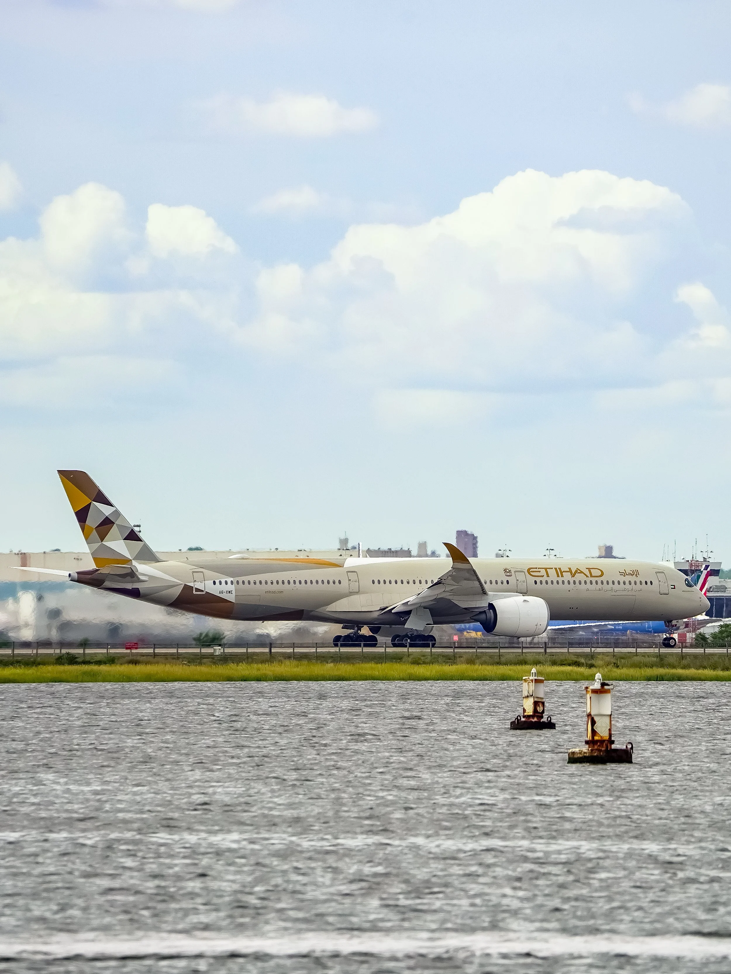 A large commercial airplane on the runway near water, with a city skyline and cloudy sky in the background.