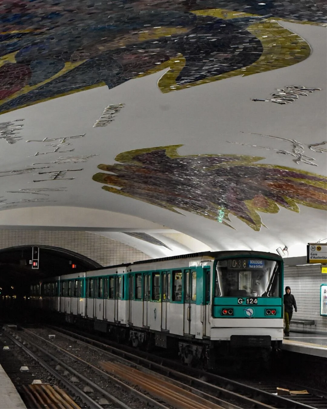 A metro train at the station with a mural of a bird painted on the ceiling.