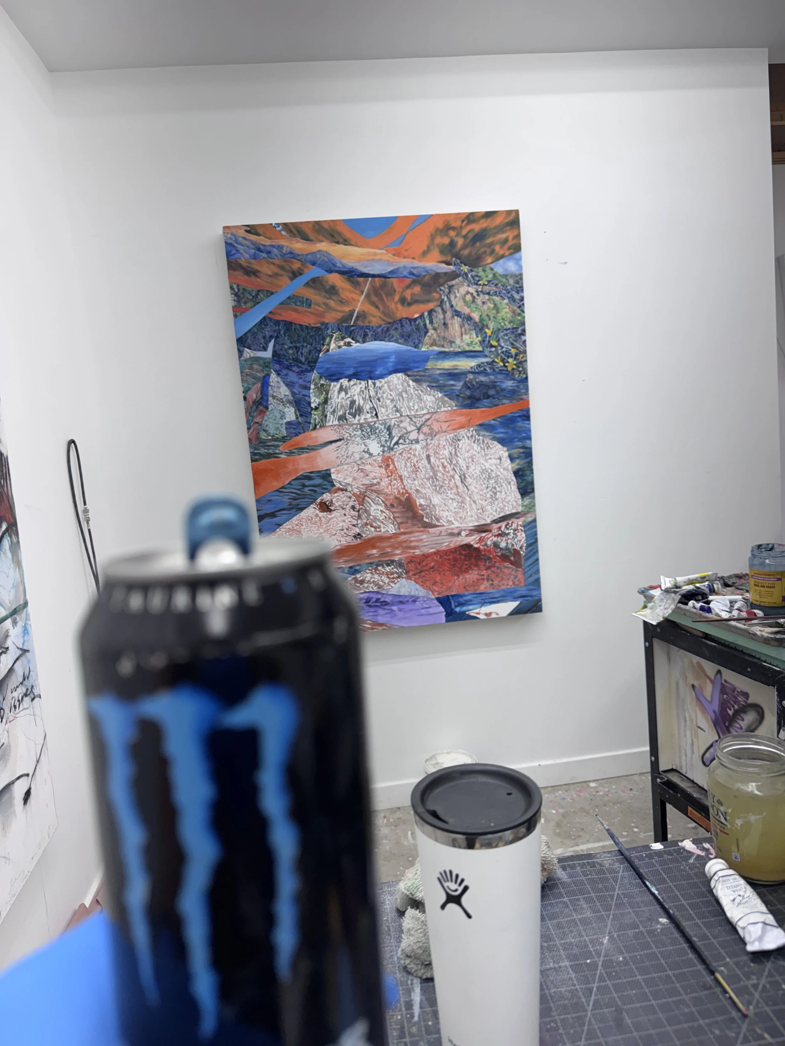 A painting on a wall in an art studio, surrounded by painting supplies, with a blurry object in the foreground.