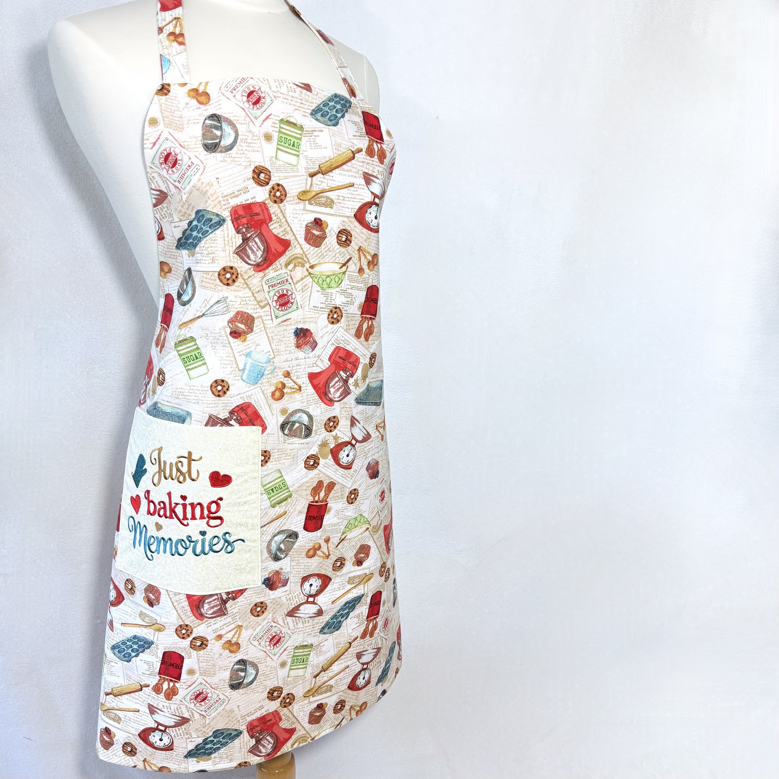 Just Baking Memories Reversible Adult bib apron on mannequin showing embroidered “Just Baking Memories” pocket and vintage baking print
