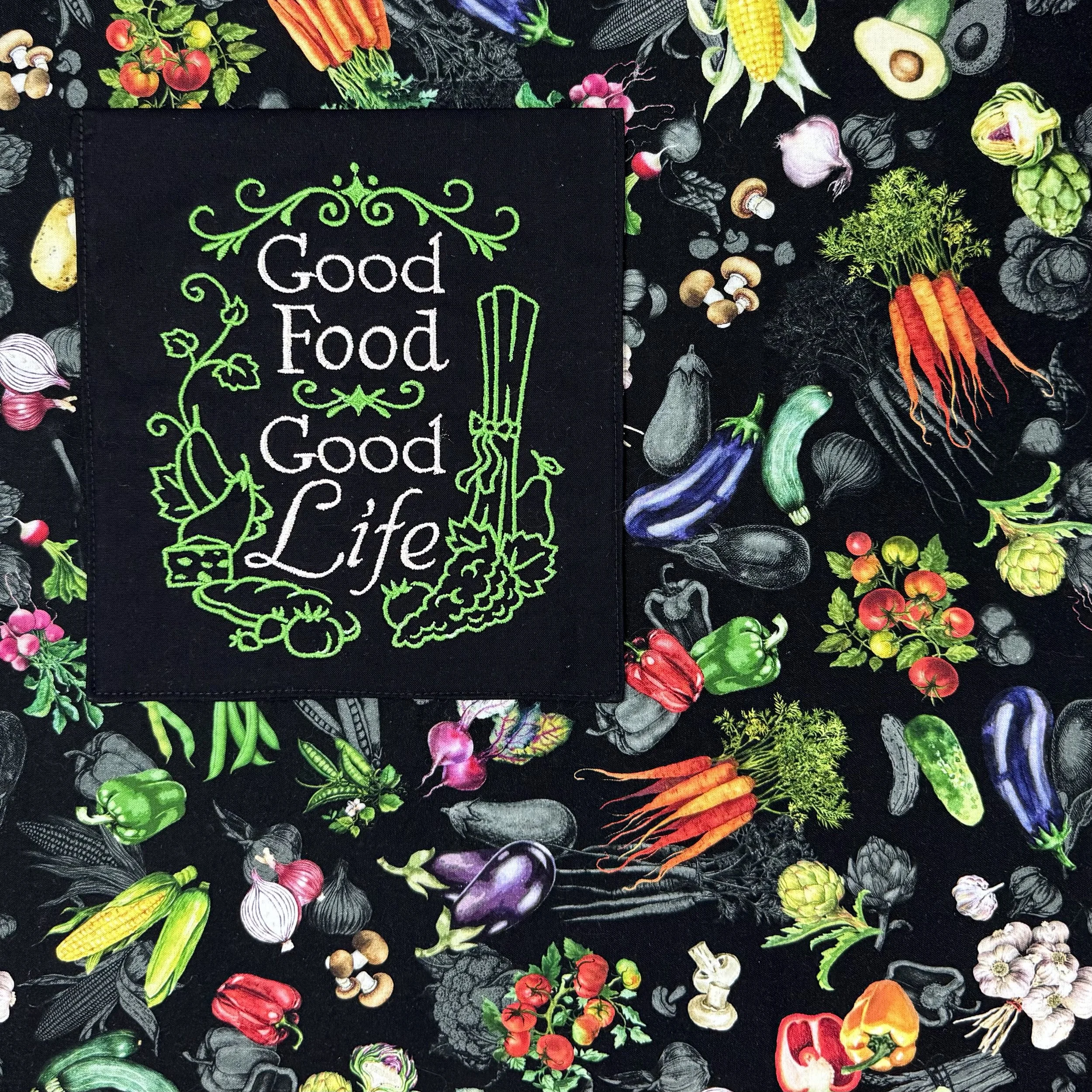Close-up of embroidered with “Good Food Good Life” framed by green vine flourishes and vegetable accents