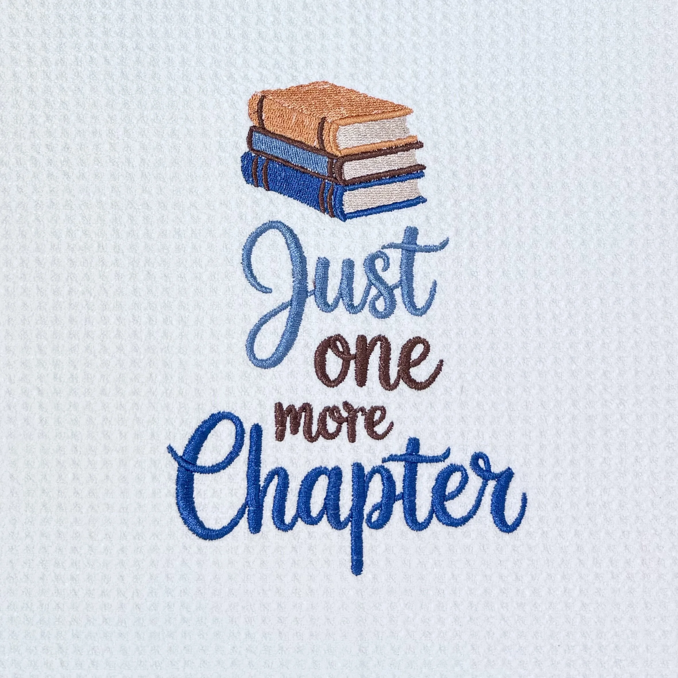 Close-up of Just One More Chapter embroidery on microfiber kitchen and hand towel, showing detailed stitching, books design, and towel texture