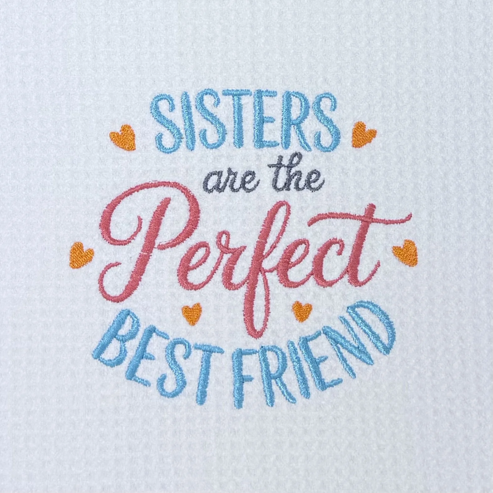Close-up of "Sisters Are The Perfect Best Friend" embroidery on microfiber kitchen and hand towel, showing aqua, coral, gray stitching, orange heart accents, and towel texture