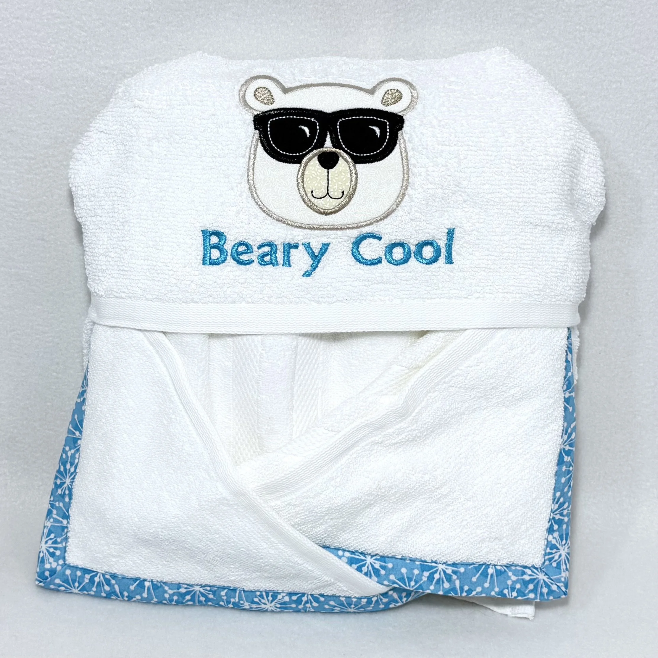 Folded beary cool hooded towel for babies and kids, showing the polar bear in sunglasses appliqué hood with “Beary cool” and coordinating easy-wrap pockets