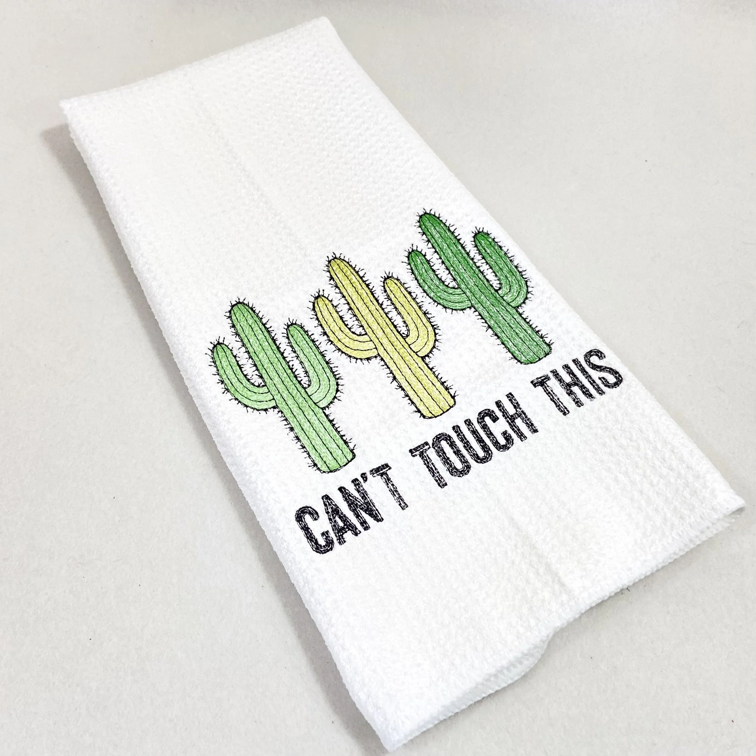 Folded white microfiber dish towel with green and yellow embroidered cactus design on white background
