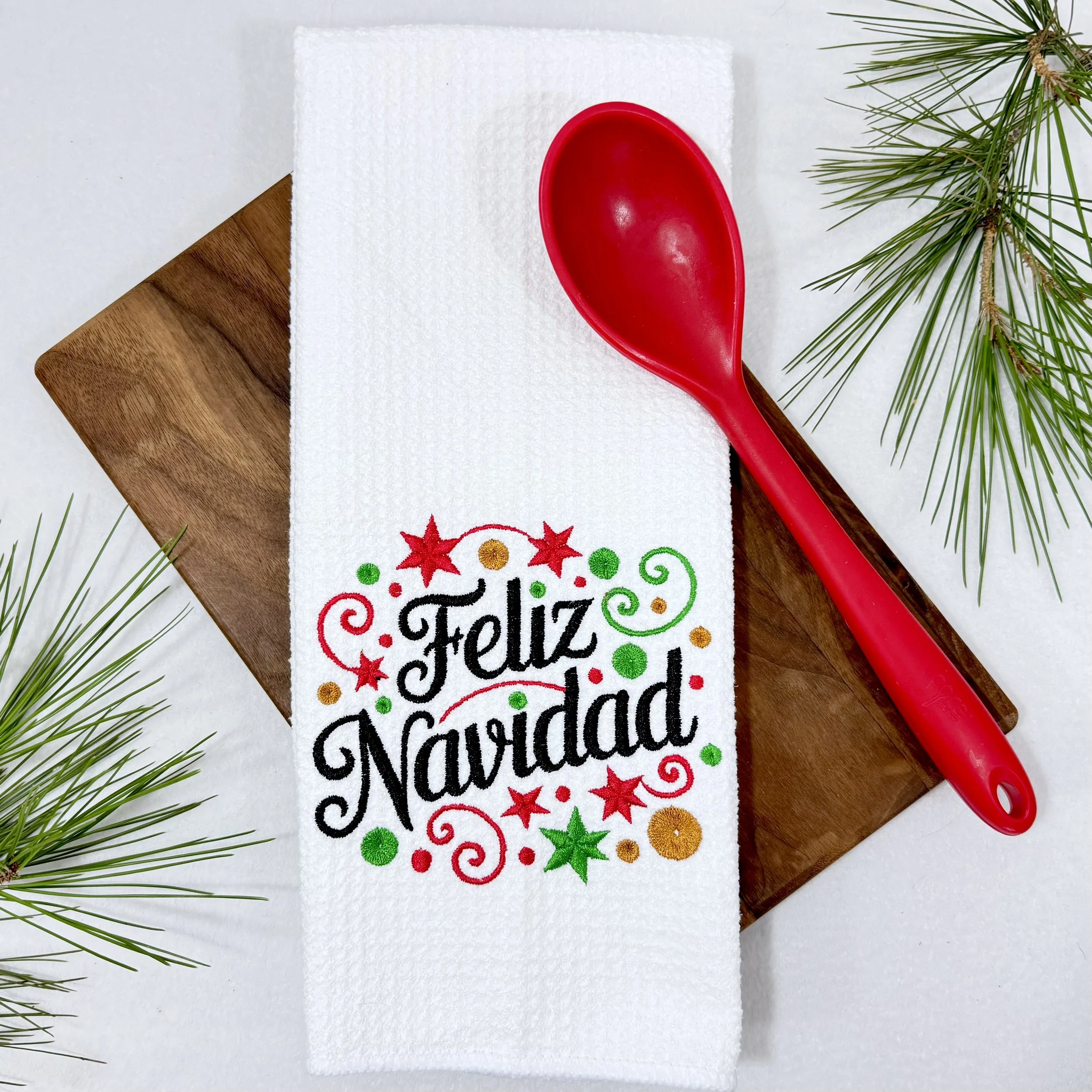 Feliz Navidad embroidered microfiber kitchen and hand towel flat lay with greenery and kitchen tools