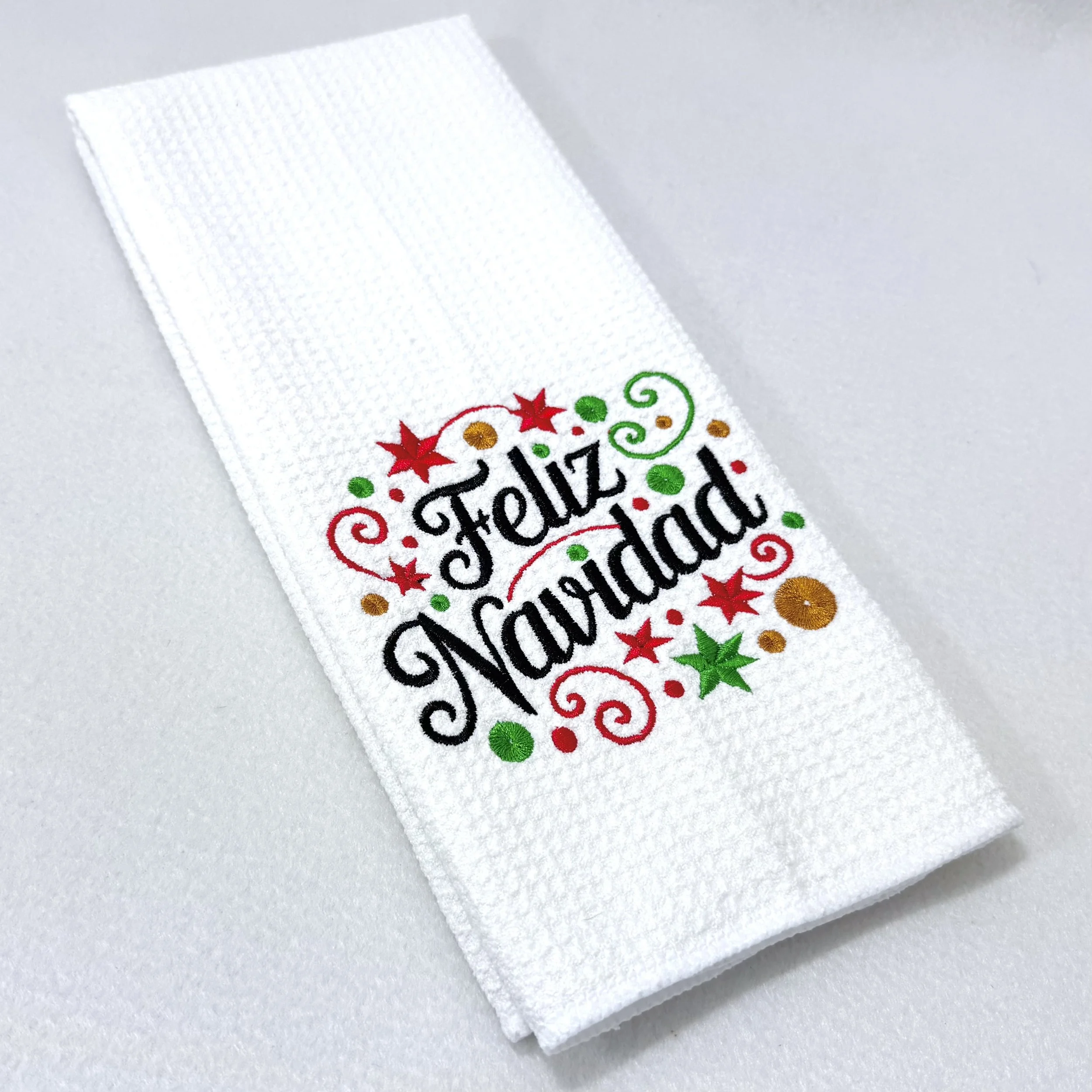 Feliz Navidad embroidered microfiber kitchen and hand towel folded on white background, showing design and texture