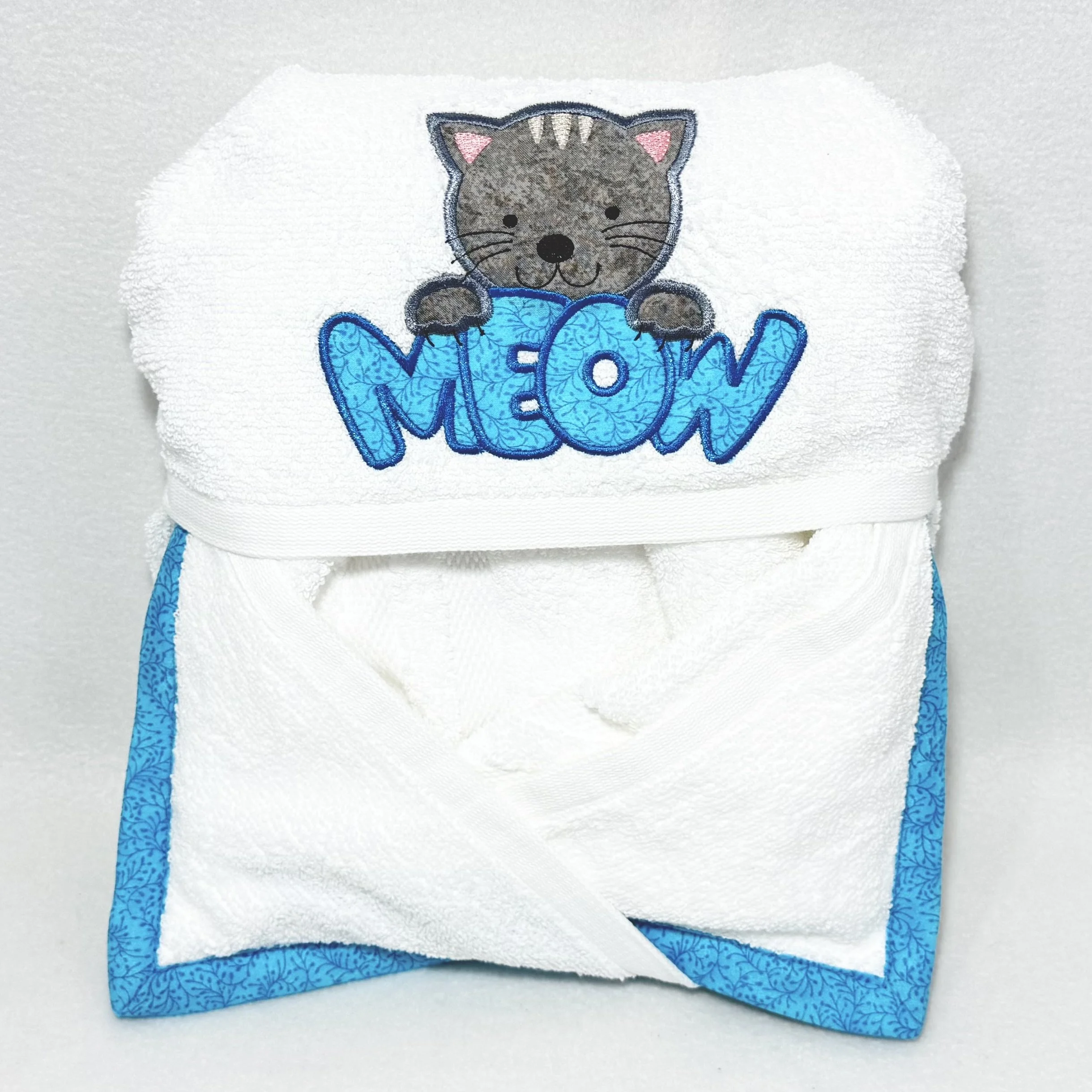 Folded meow cat hooded towel for babies and kids, showing the gray cat with teal meow appliqué hood and coordinating easy-wrap pockets
