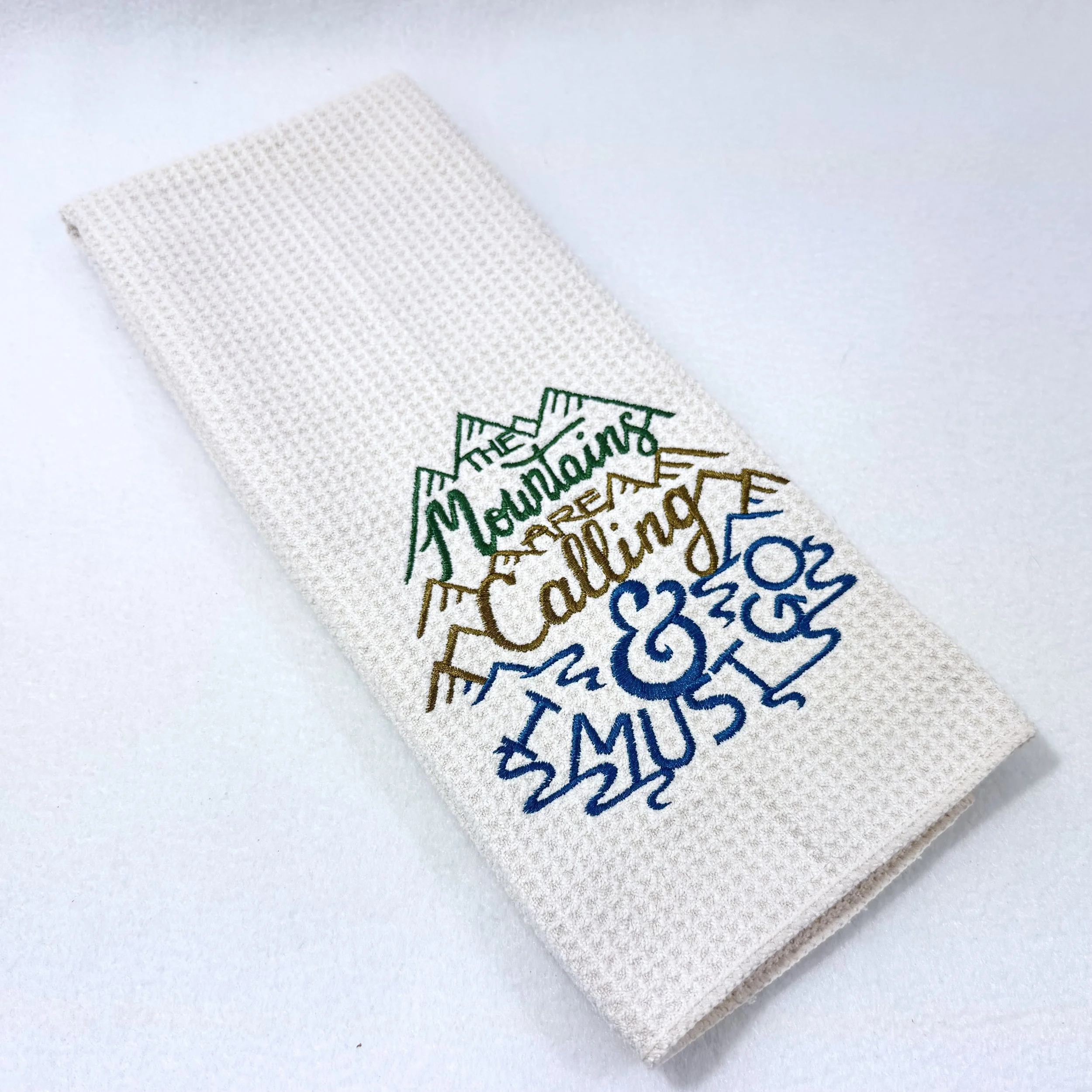 The Mountains Are Calling & I Must Go embroidered microfiber kitchen and hand towel folded on white background, showing mountain design and texture
