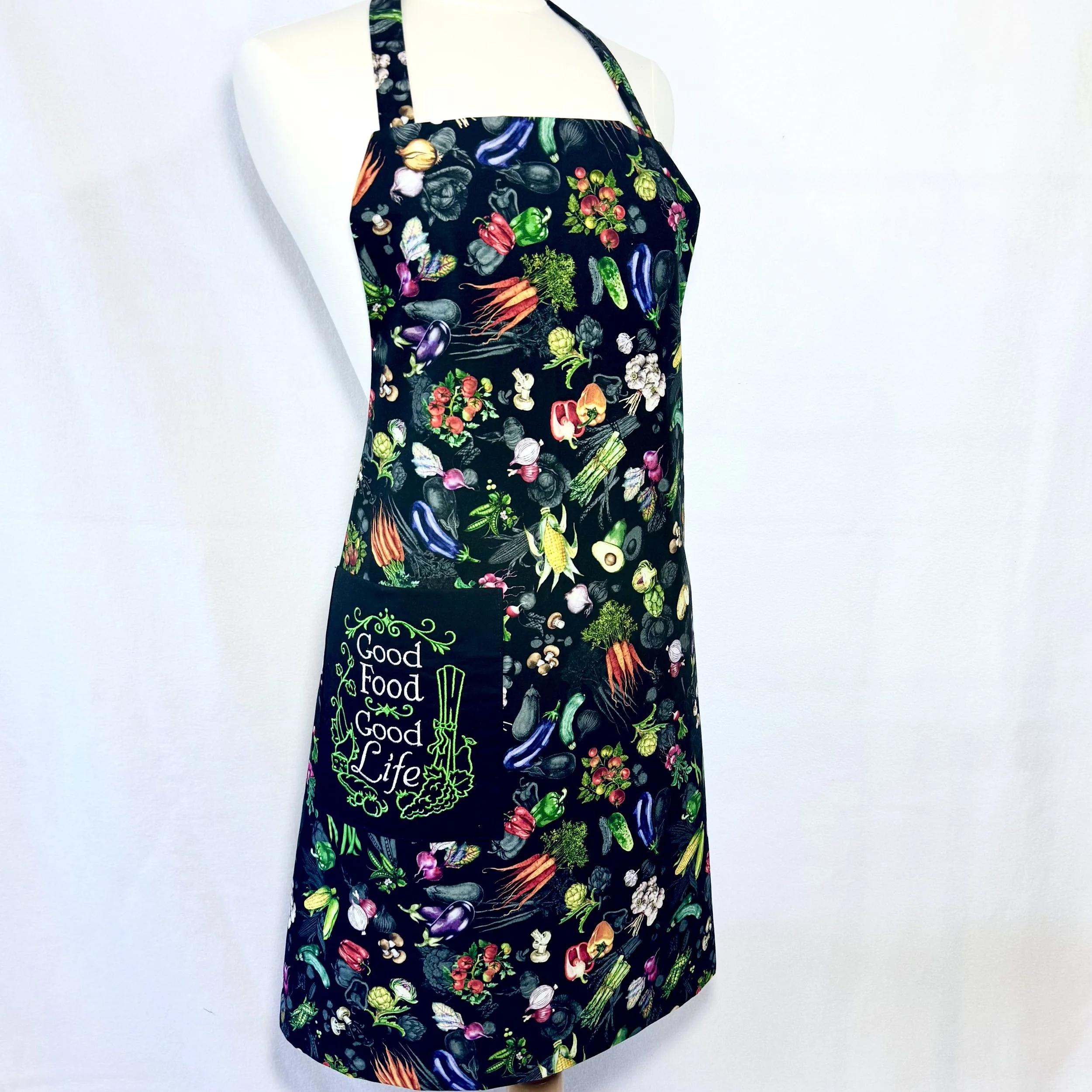 Good Food Good Life Reversible Adult bib apron on mannequin showing embroidered “good food good life” pocket and garden vegetable print