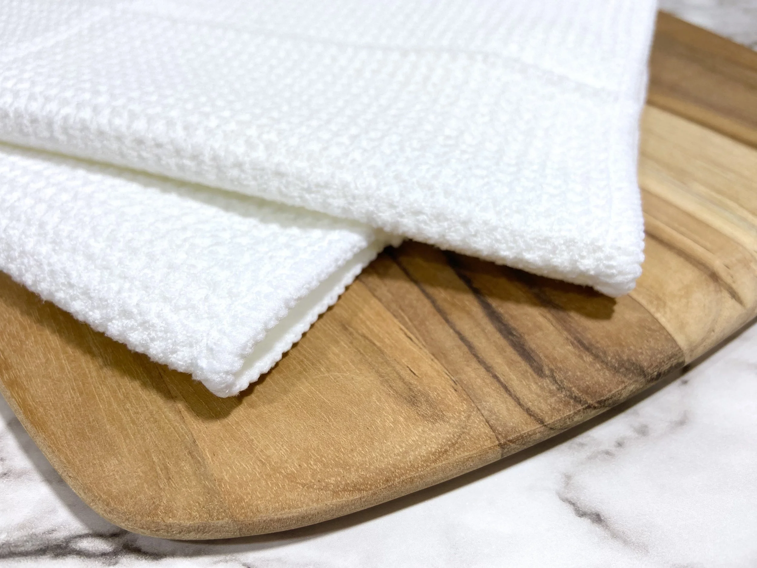 Close-up of white microfiber kitchen and hand towel edge and waffle weave texture, showing high-quality material and embroidered detail