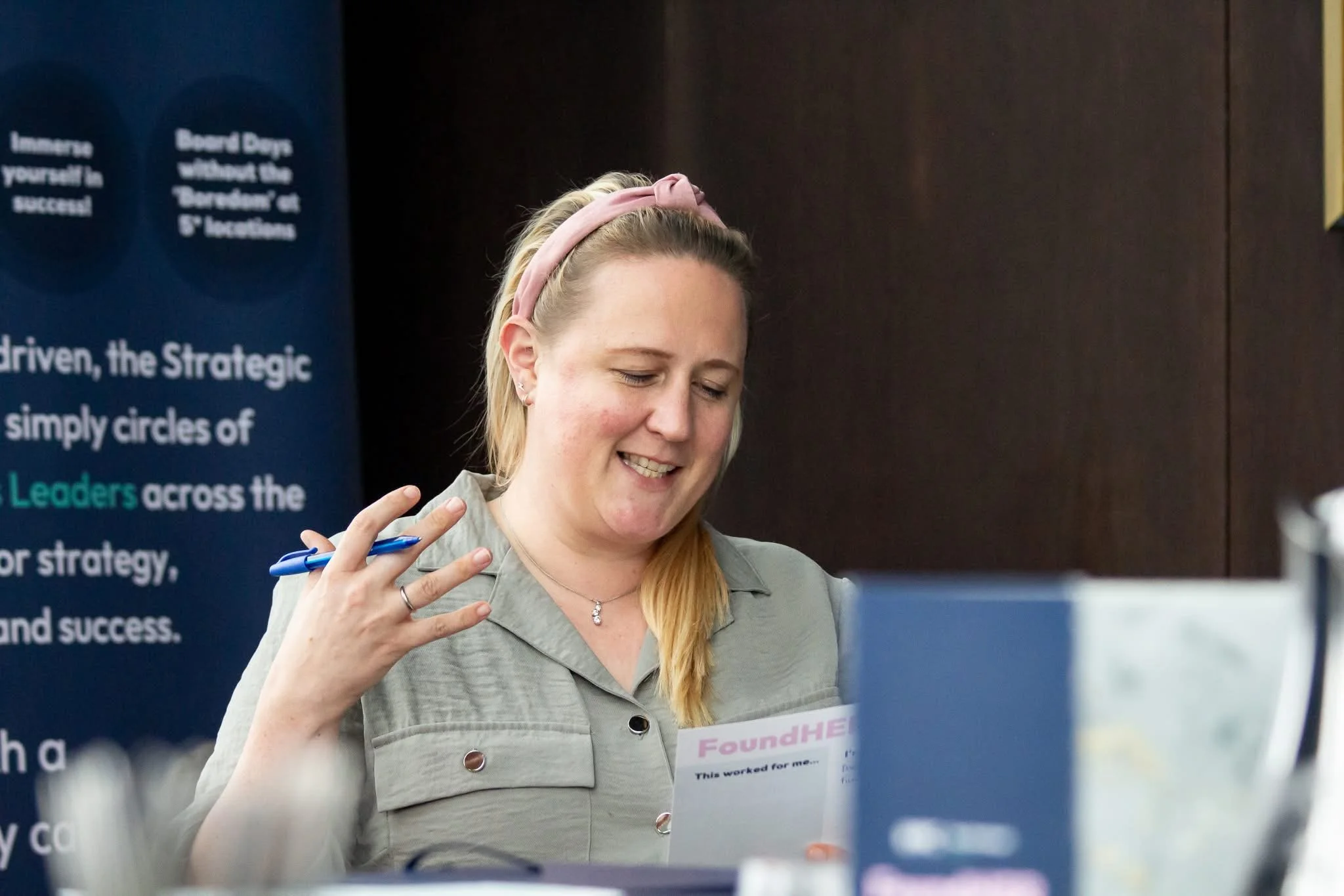 A woman in a meeting, smiling, wearing a pink hairband