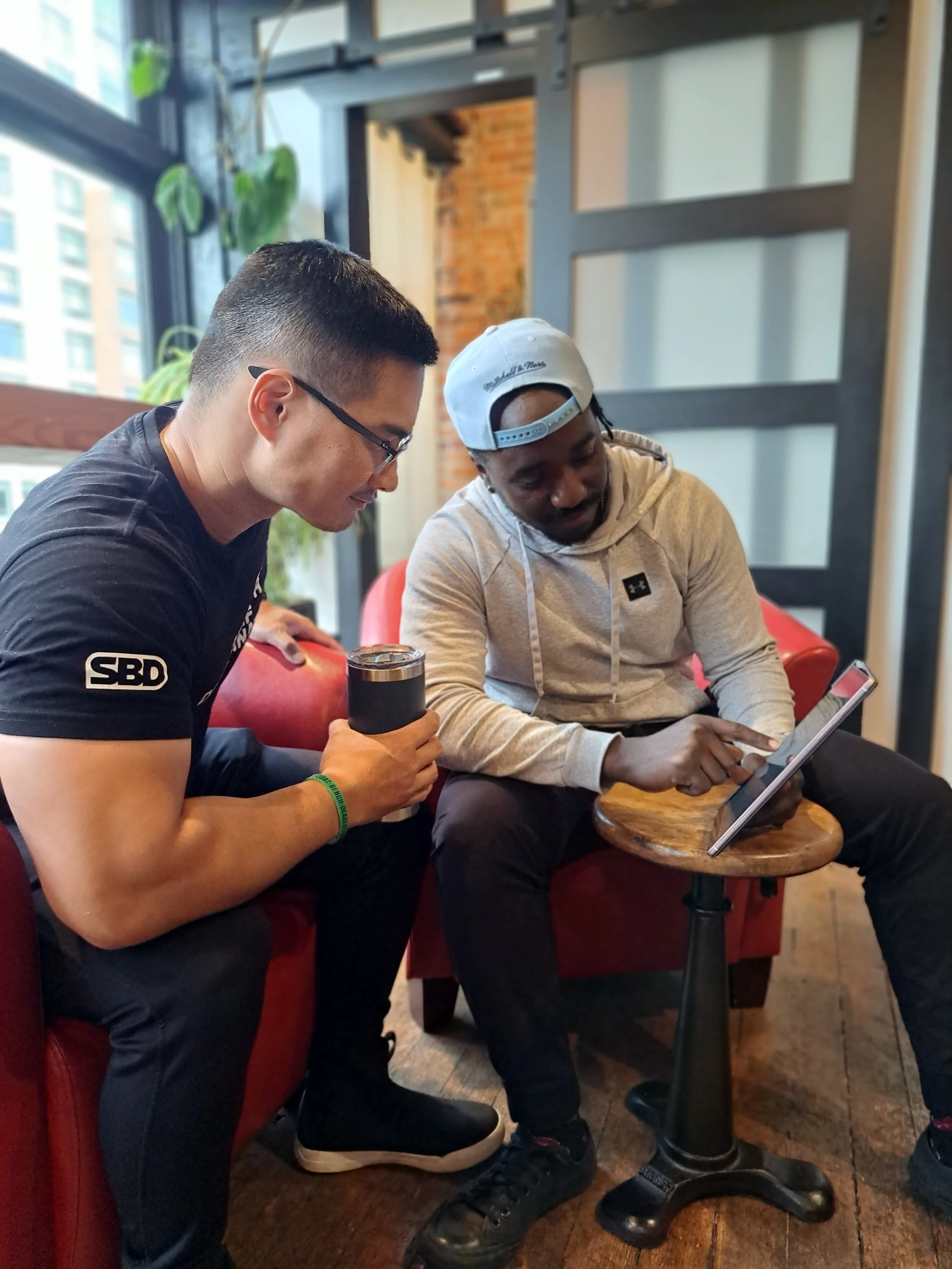 Two personal trainersd sit on bright red chairs looking at a tablet.