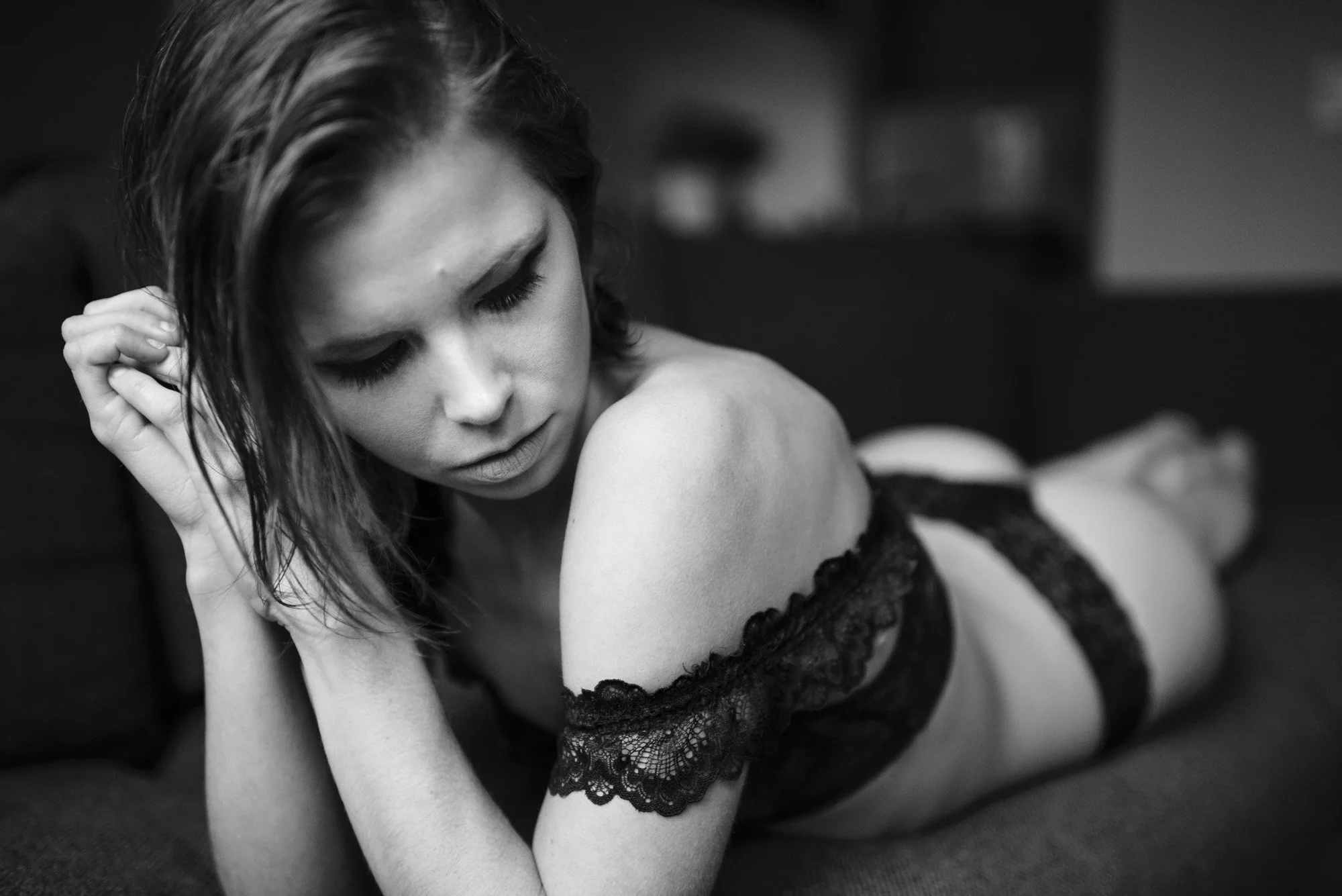 A woman in lace lingerie lying on a sofa with her eyes closed, black and white photo.