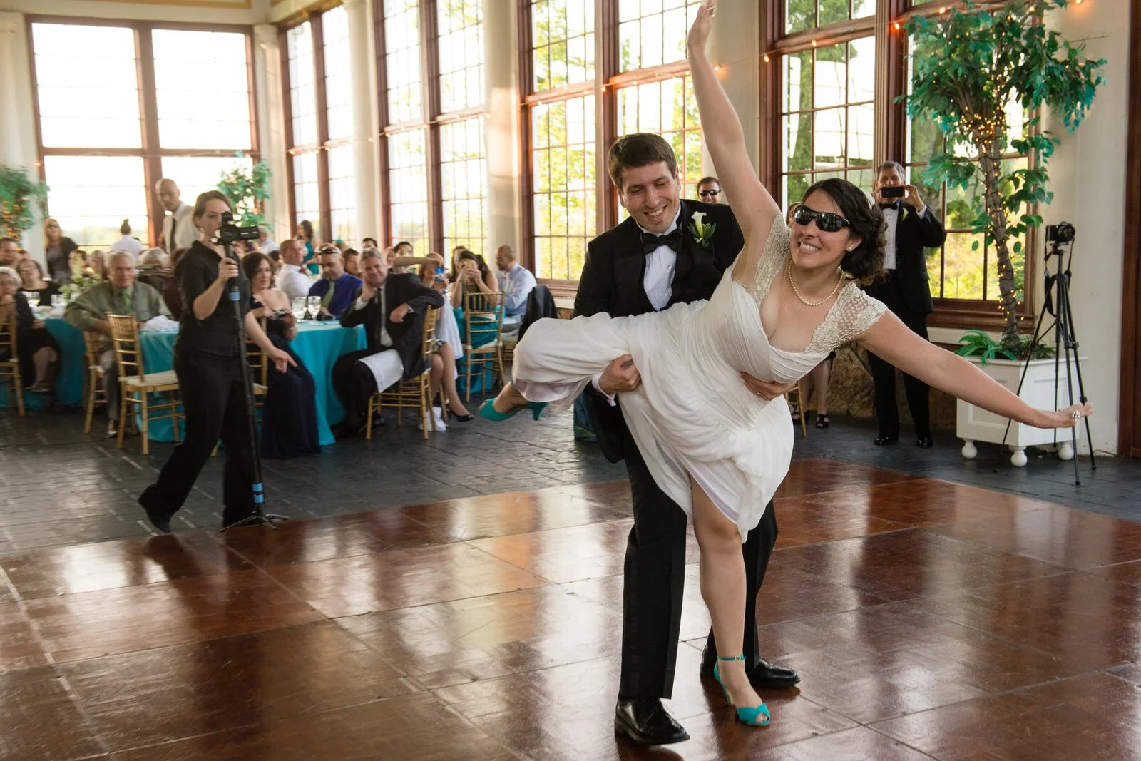A couple, dressed in wedding attire, dancing at a wedding reception with guests seated at tables watching and taking pictures.