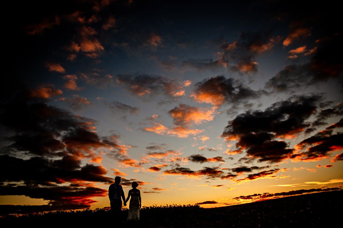 Silhouettes of a couple holding hands under a colorful, dramatic sunset sky with clouds.