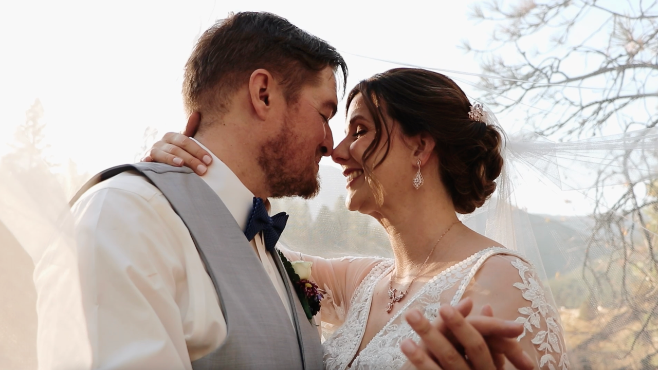 Romantic outdoor wedding portrait of a couple sharing an intimate forehead-to-forehead moment in a mountain setting.