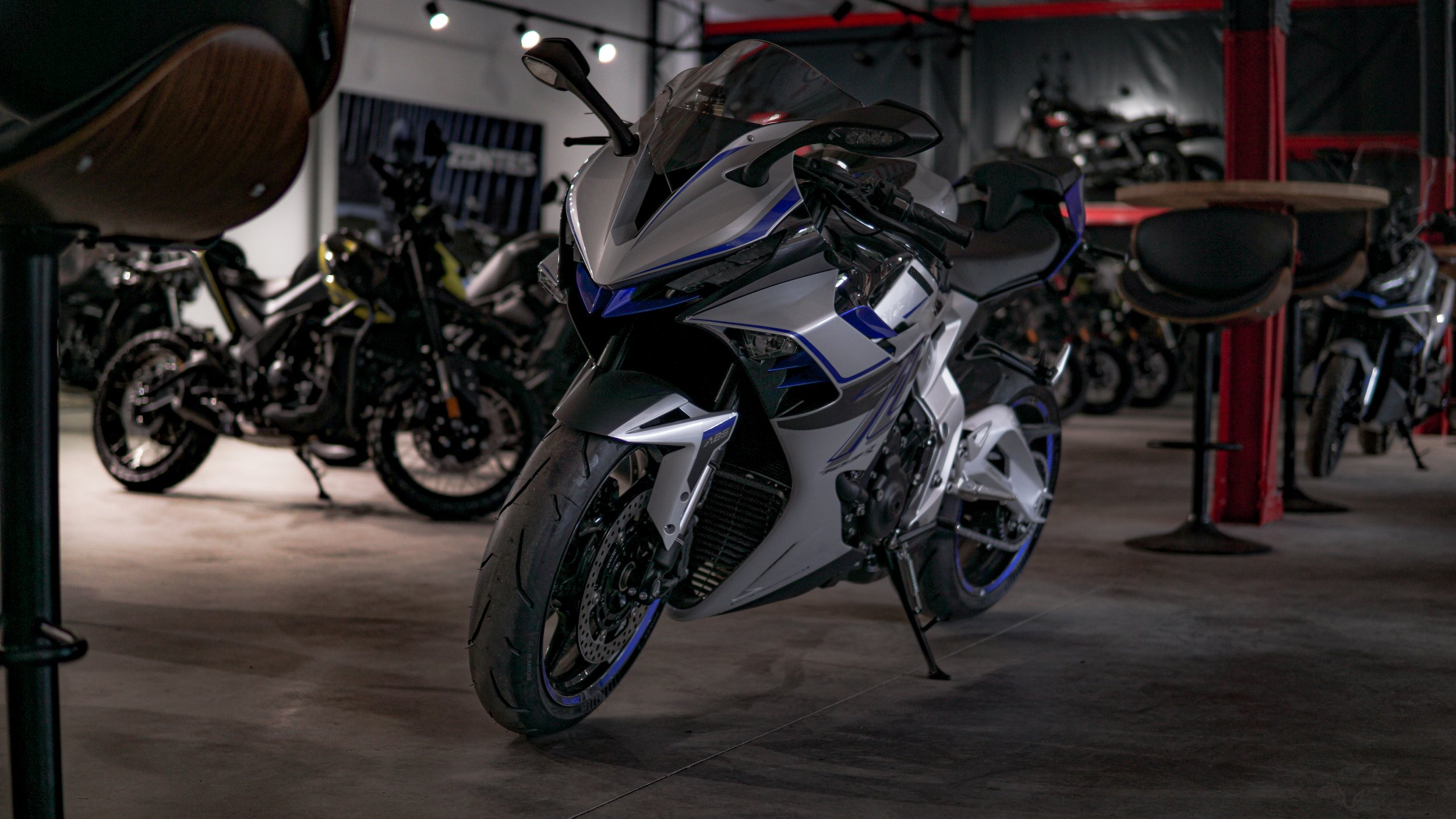 A sleek, white and blue sport motorcycle displayed in a showroom, surrounded by other motorcycles and accessories.