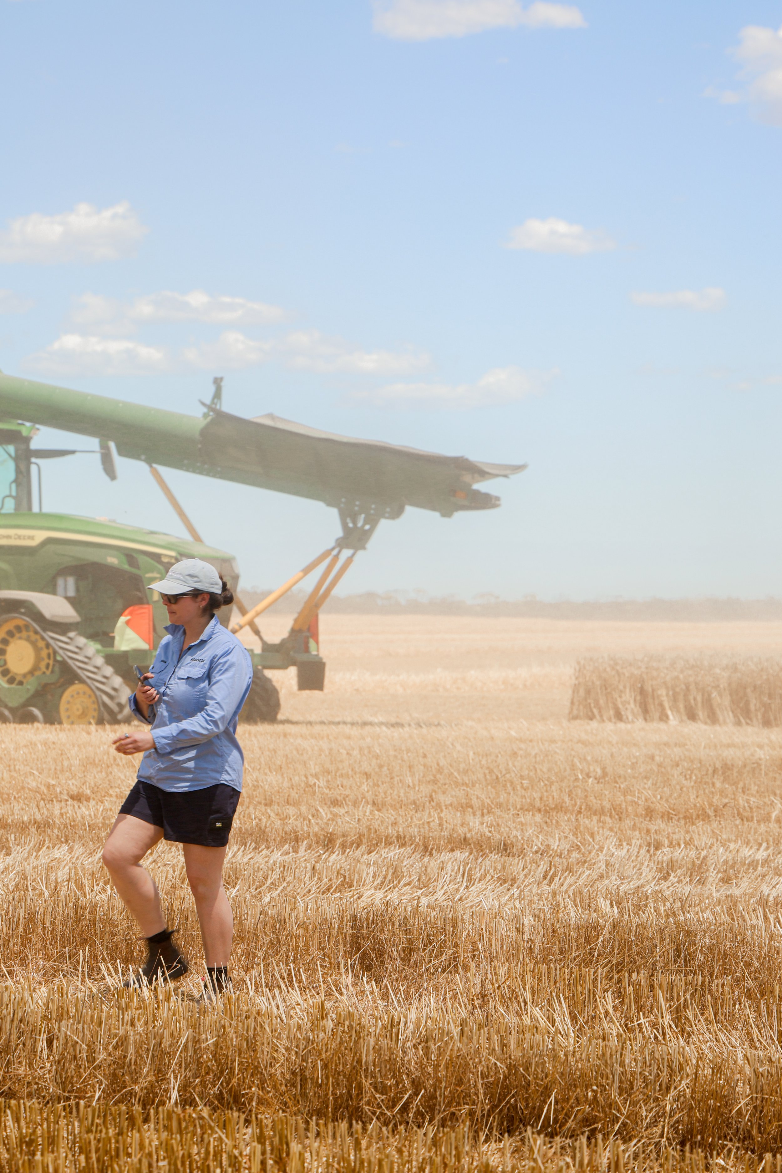 Two people walking through a rural landscape with open fields and scattered trees, one person filming with a camera and the other holding papers, under a partly cloudy sky — representing AGSOCIAL’s on-farm strategy and content production in agricultu