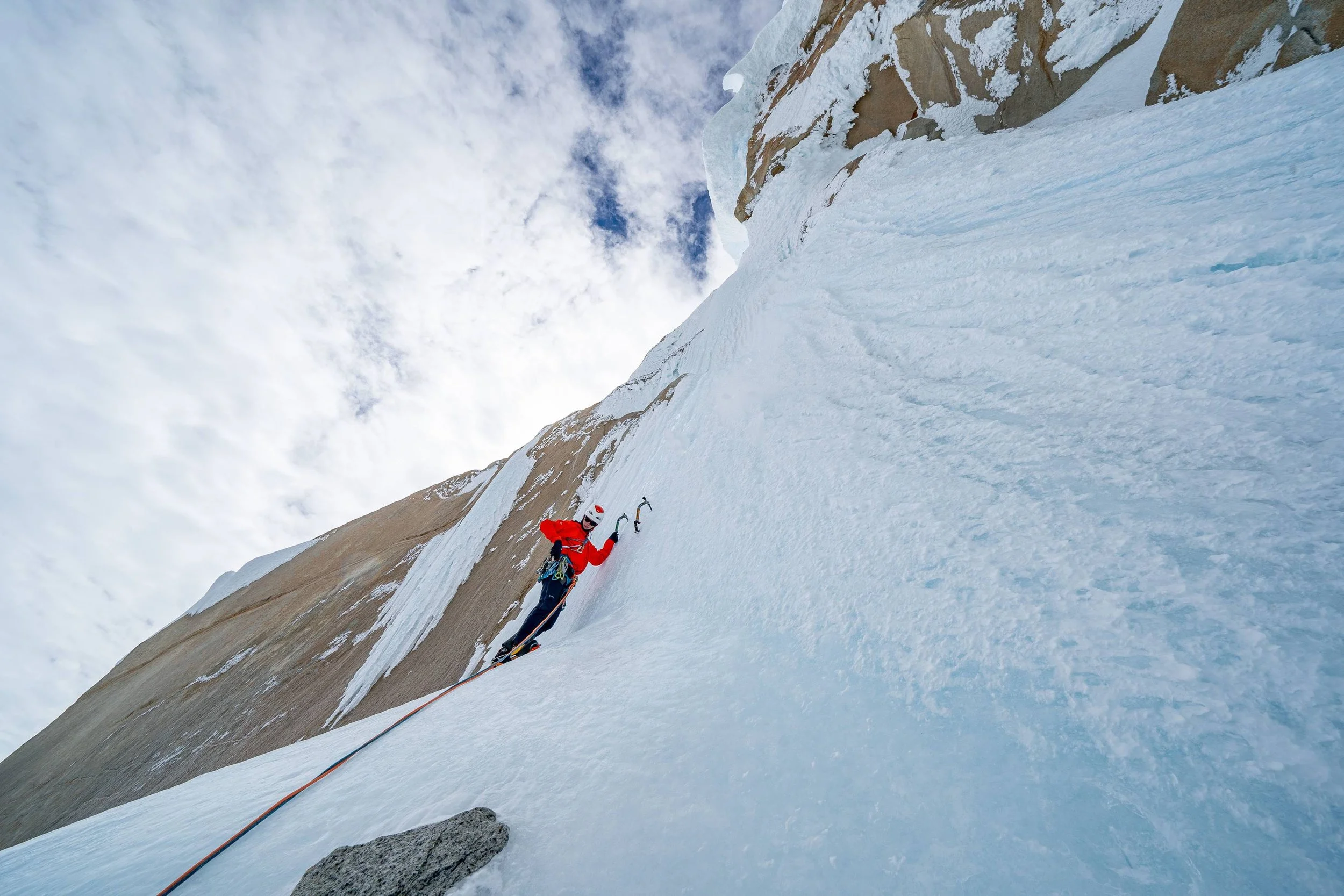 Kletterer beim Eisklettern an einer gefrorenen Felswand in der Berge, getragen mit Eiskletterausrüstung, vom Boden aus aufgenommen.