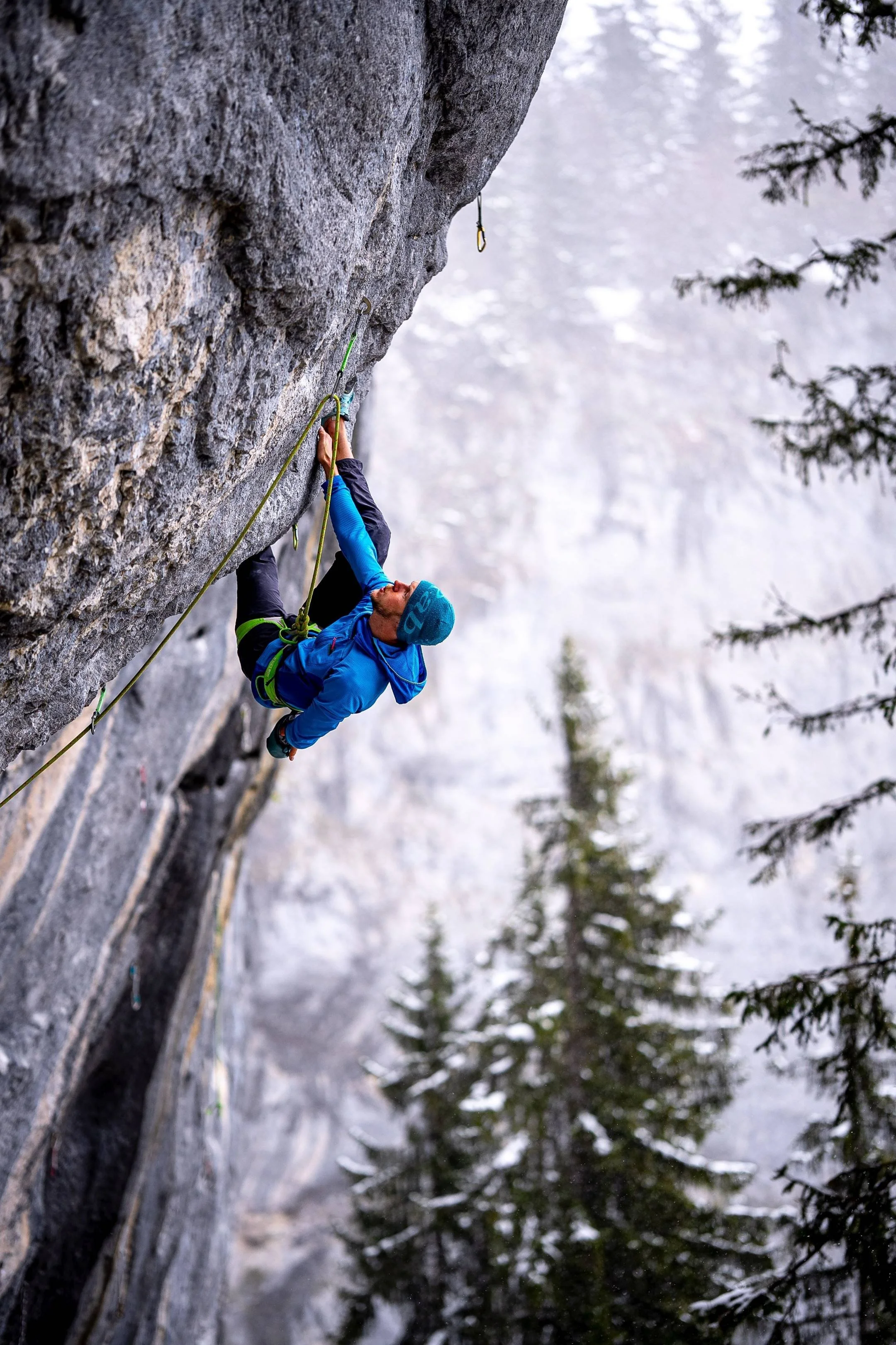 Kletterer in blauer Jacke und Mütze klettert an Felsformation in winterlicher Berglandschaft.