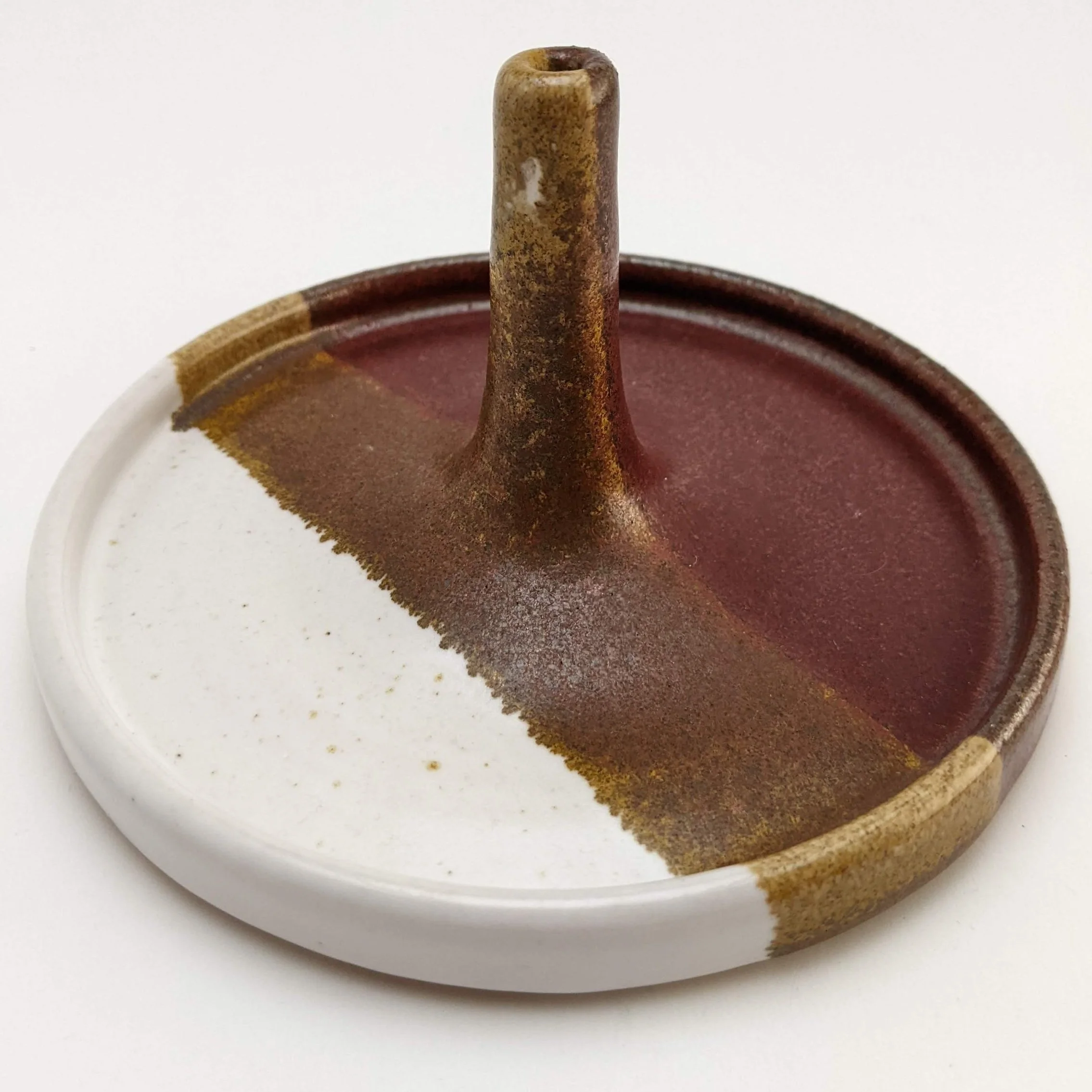 Close-up of a brown and beige ceramic object with a narrow, tube-like protrusion on a white surface.