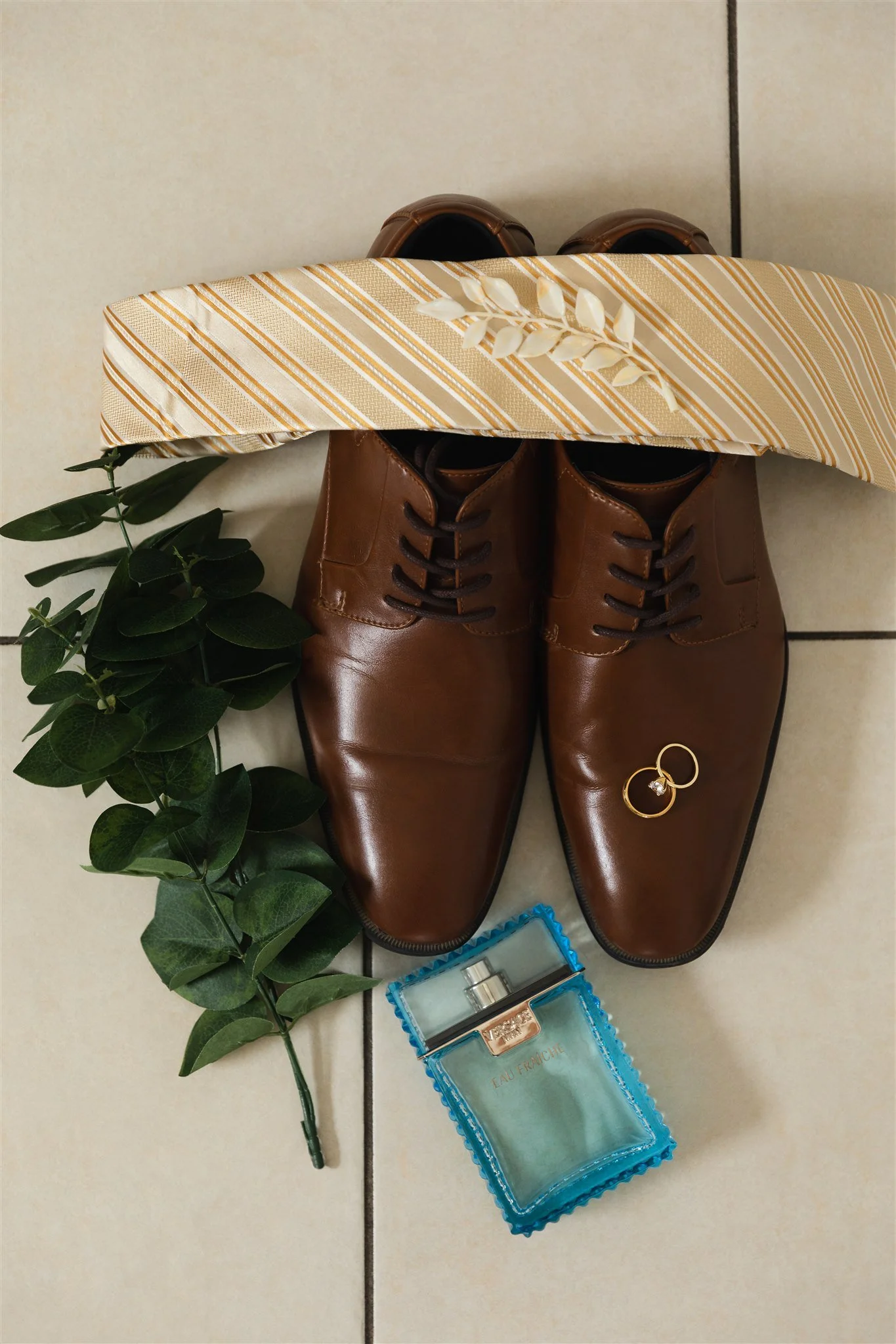 flay lay view of groom details such as wedding shoes, wedding bands, cologne and tie with a few additional decorations