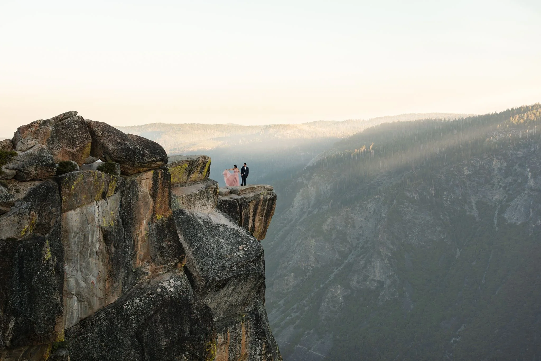 Couple in Yosemite Taft Point cliffs overlooking the valley during sunrise. They wear formal gown and tux