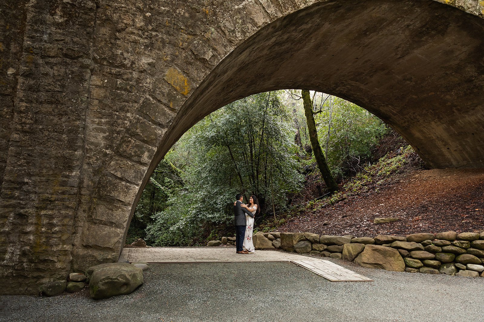 Engaged couple dances under rustic bridge at Saratoga Spring Wedding center in the Bay Area