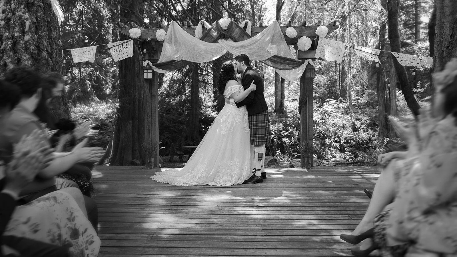 A couple celebrates with their guests after eloping, they stand under a decorated wooden frame surrounded by tall redwoods trees in Mt Hood Oregon