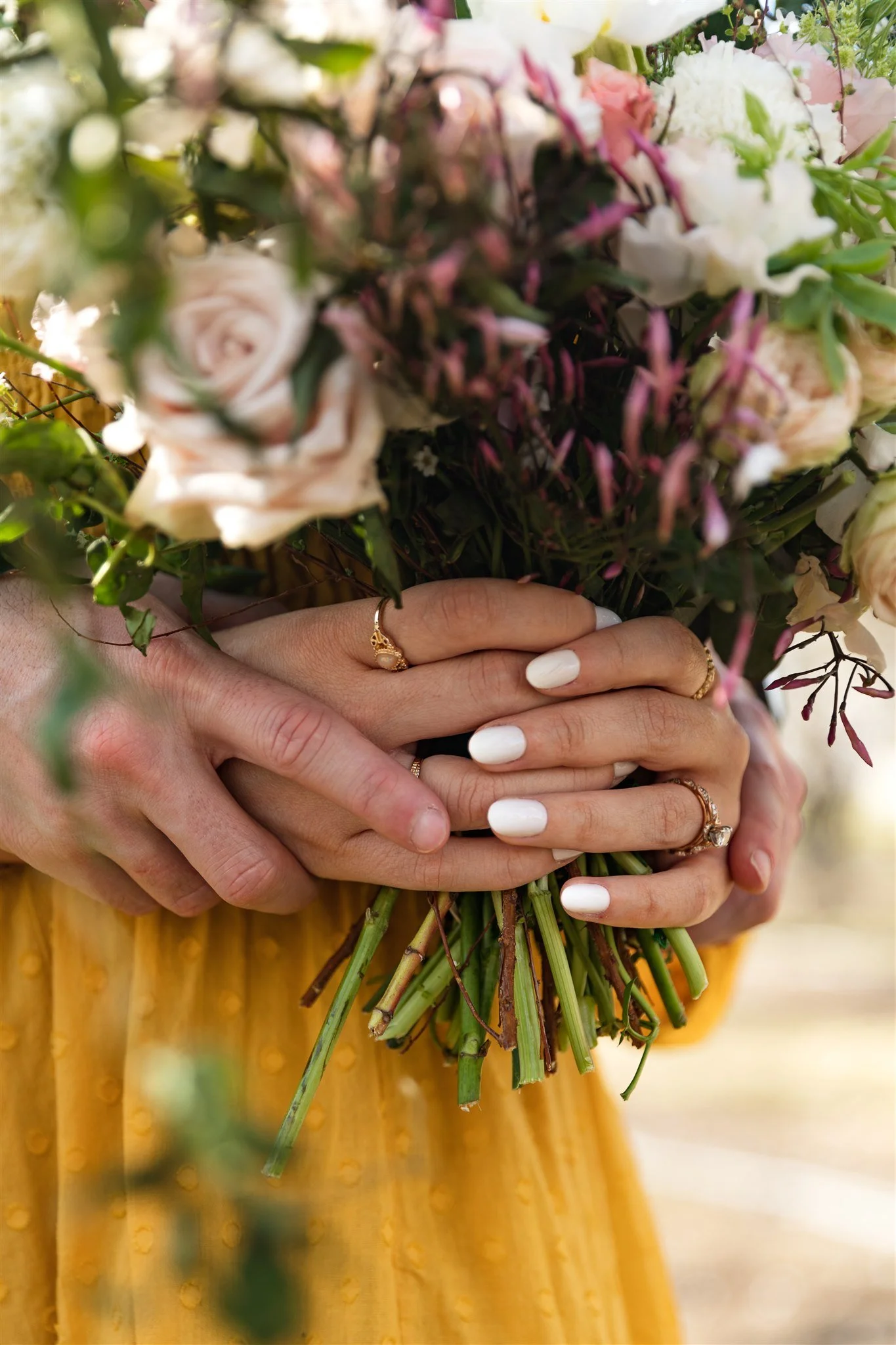 Engaged couple hold hands and a bouquet to show off their engagement ring
