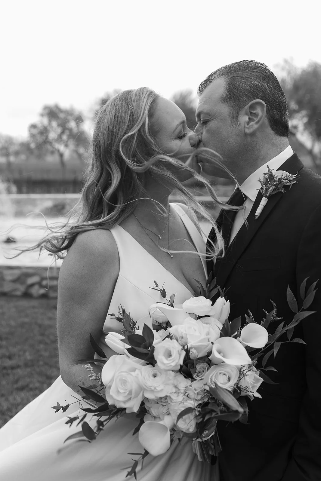 Older couple kiss passionately, and the wind blows the bride's hair, during their intimate elopement with guests