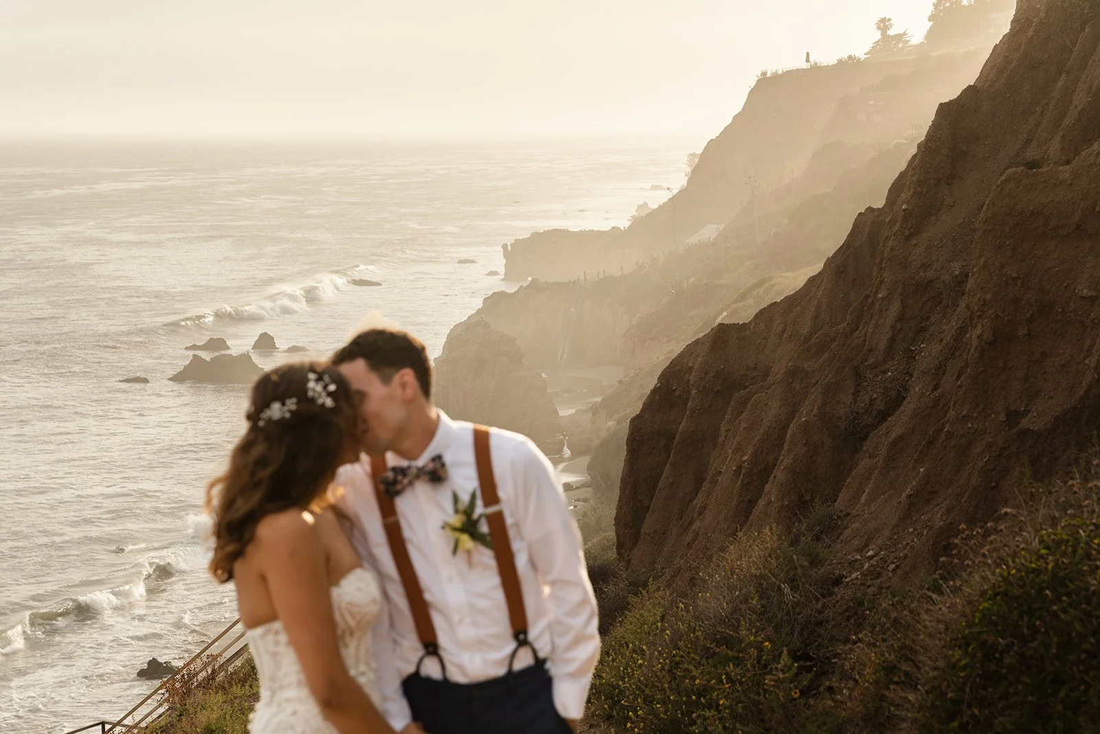 Couple kiss during sunset against the rugged cliffs of El Matador Beach and the busy waves of the ocean
