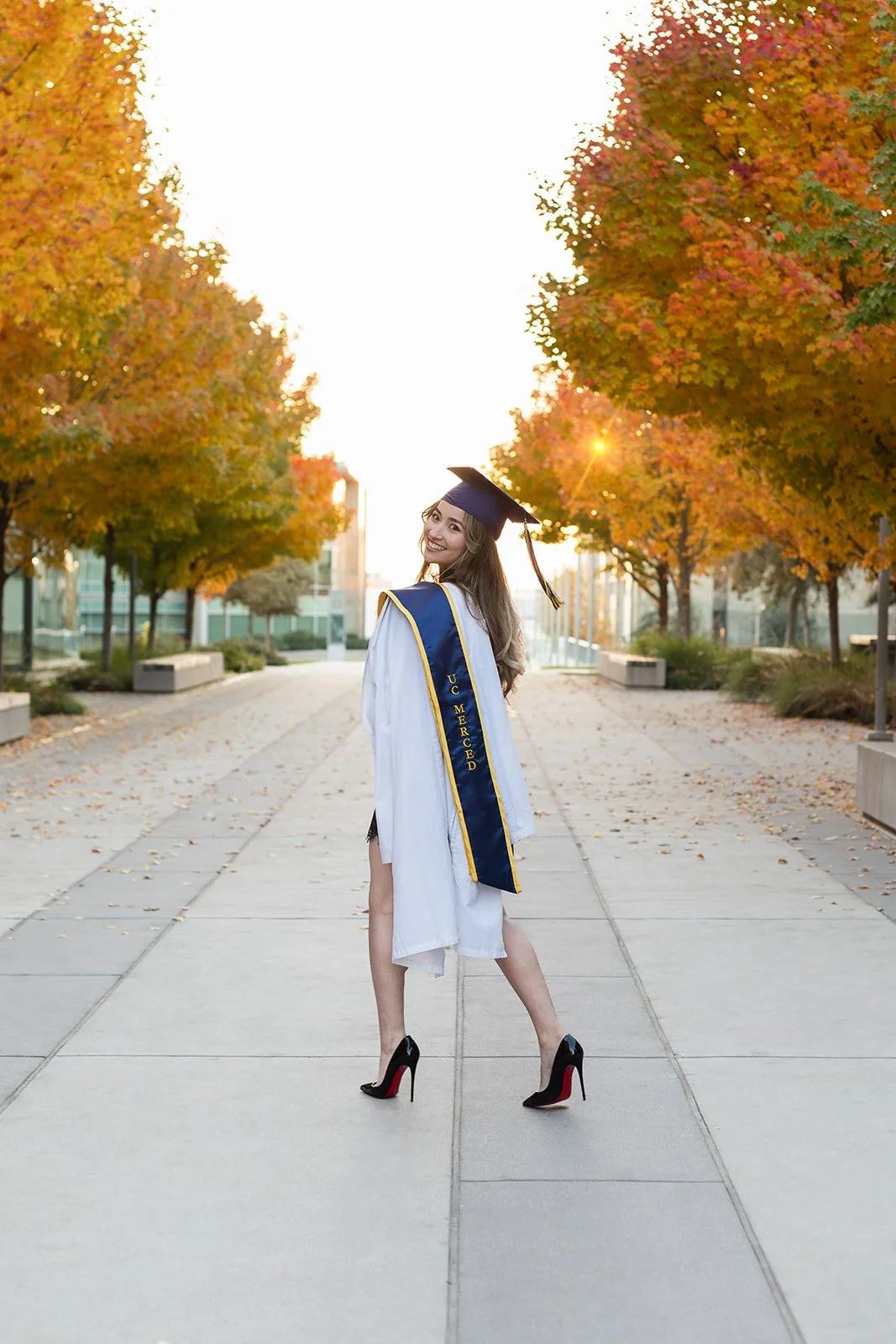 graduating senior in college poses for photo with cap and gown on campus at uc merced in california
