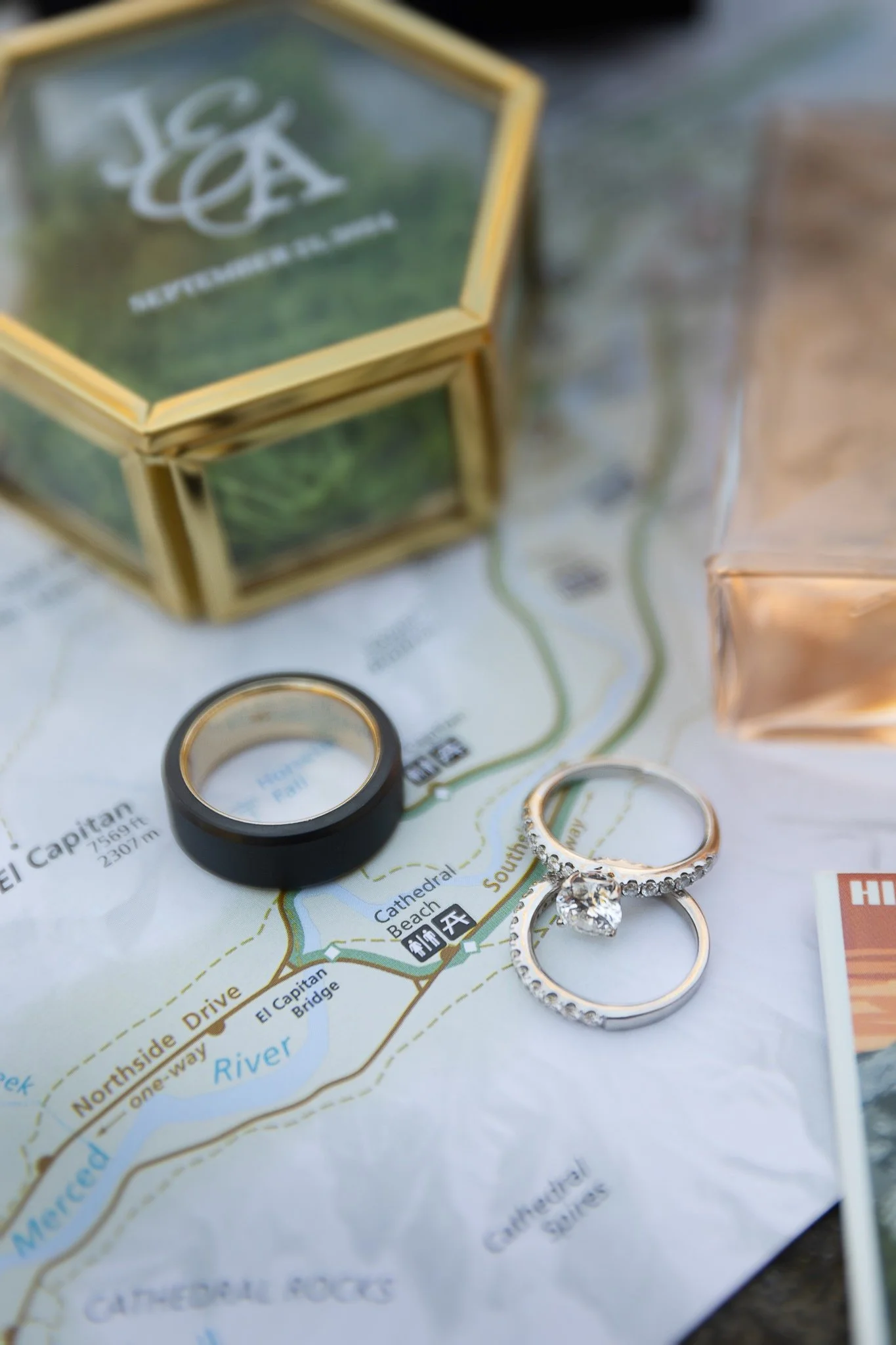 close up of wedding rings laying on top of Yosemite National Park map where couple chose to elope. A ringbox can be seen in the background