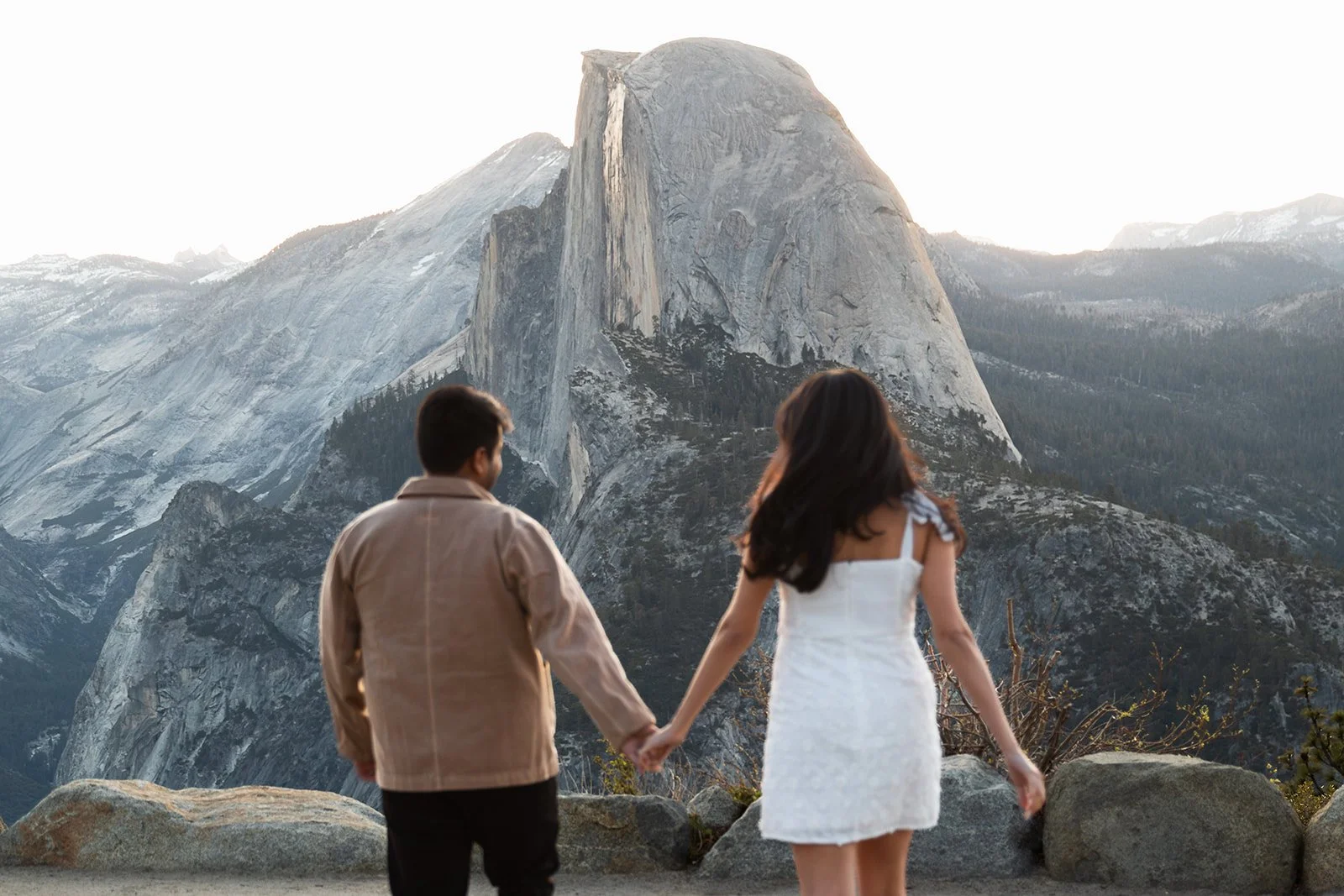 engaged couple runs hand in hand towards half dome view from glacier point