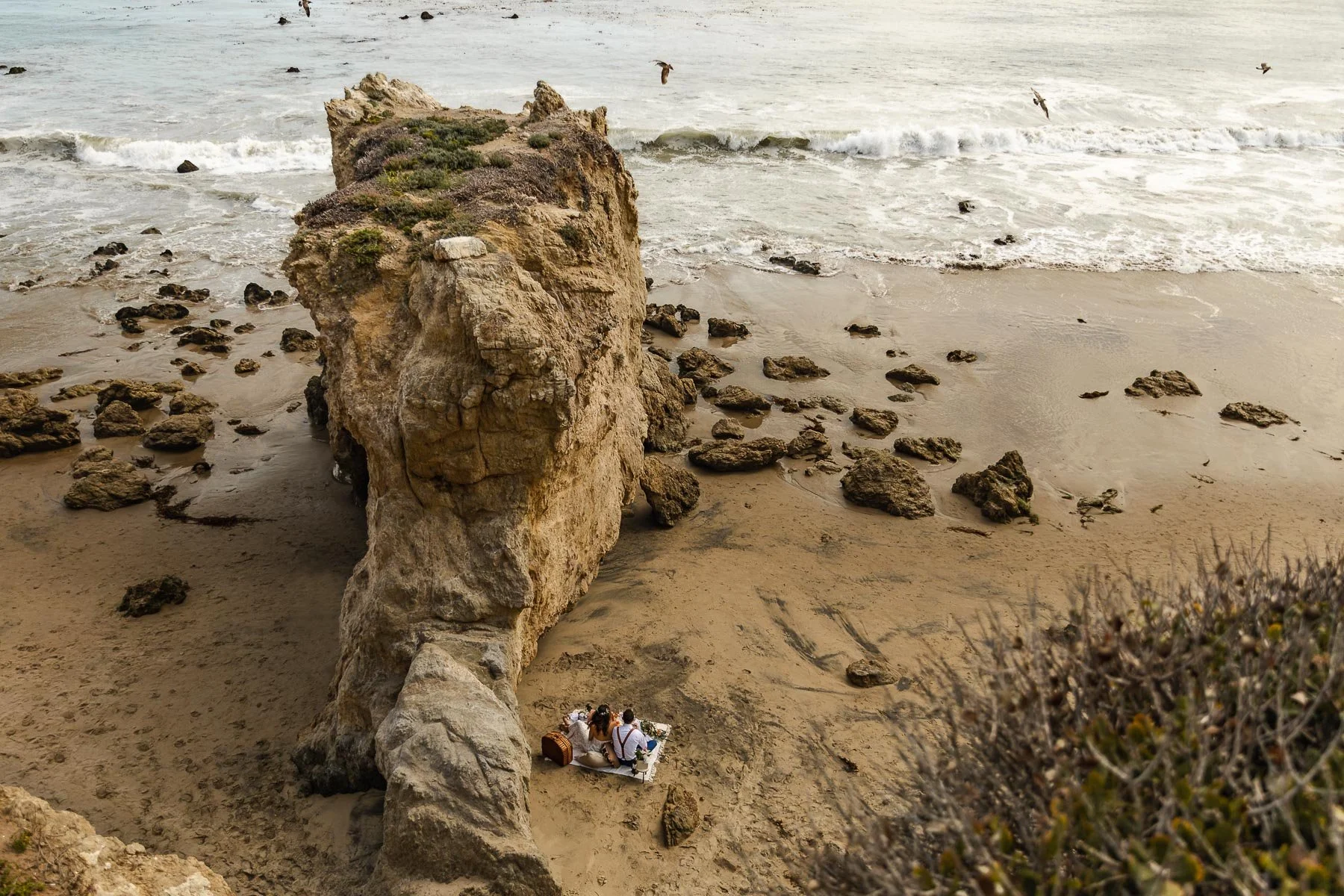 Couple elope and have a picnic at the beach in Malibu. The birds, ocean, and rocky formations are surrounding the couple
