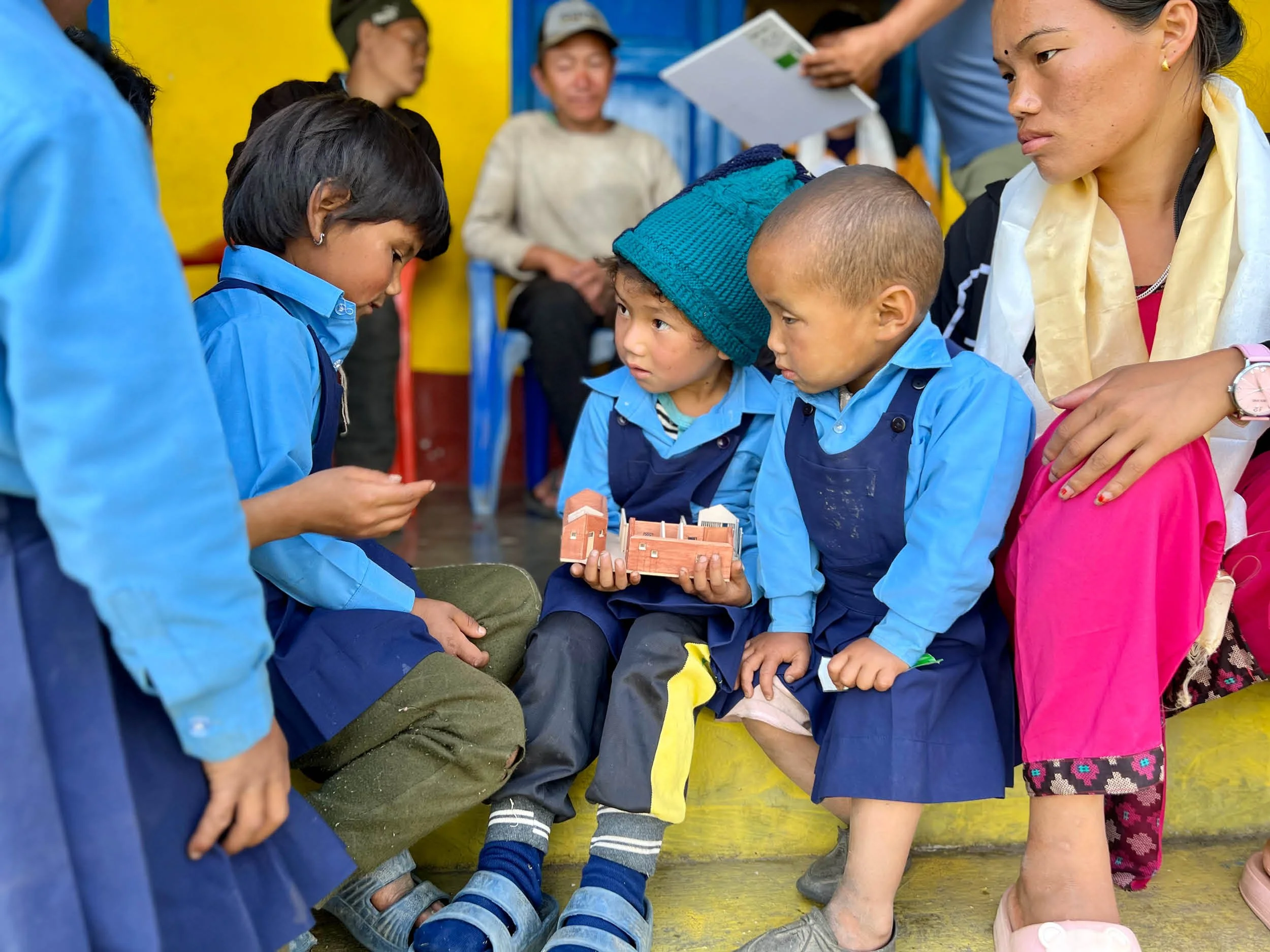 Nepali school children dressed in blue uniforms look at the model of the Ekuwa Health Post. 