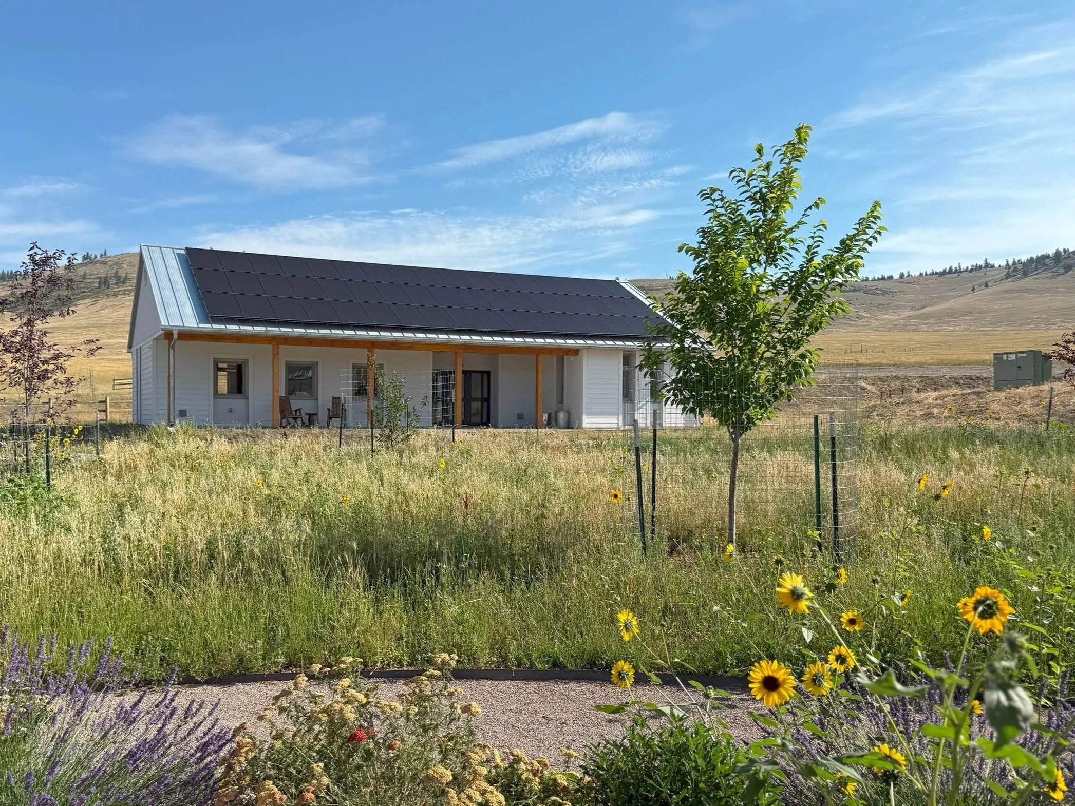 The Welcome House with solar panels on the roof set among the flowers of the Guru Rinpoche Park in rural Montana.
