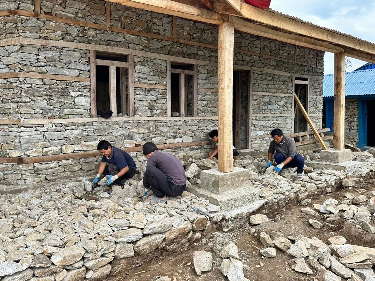 Four villagers work on the stone construction of the Ekuwa Health Post.