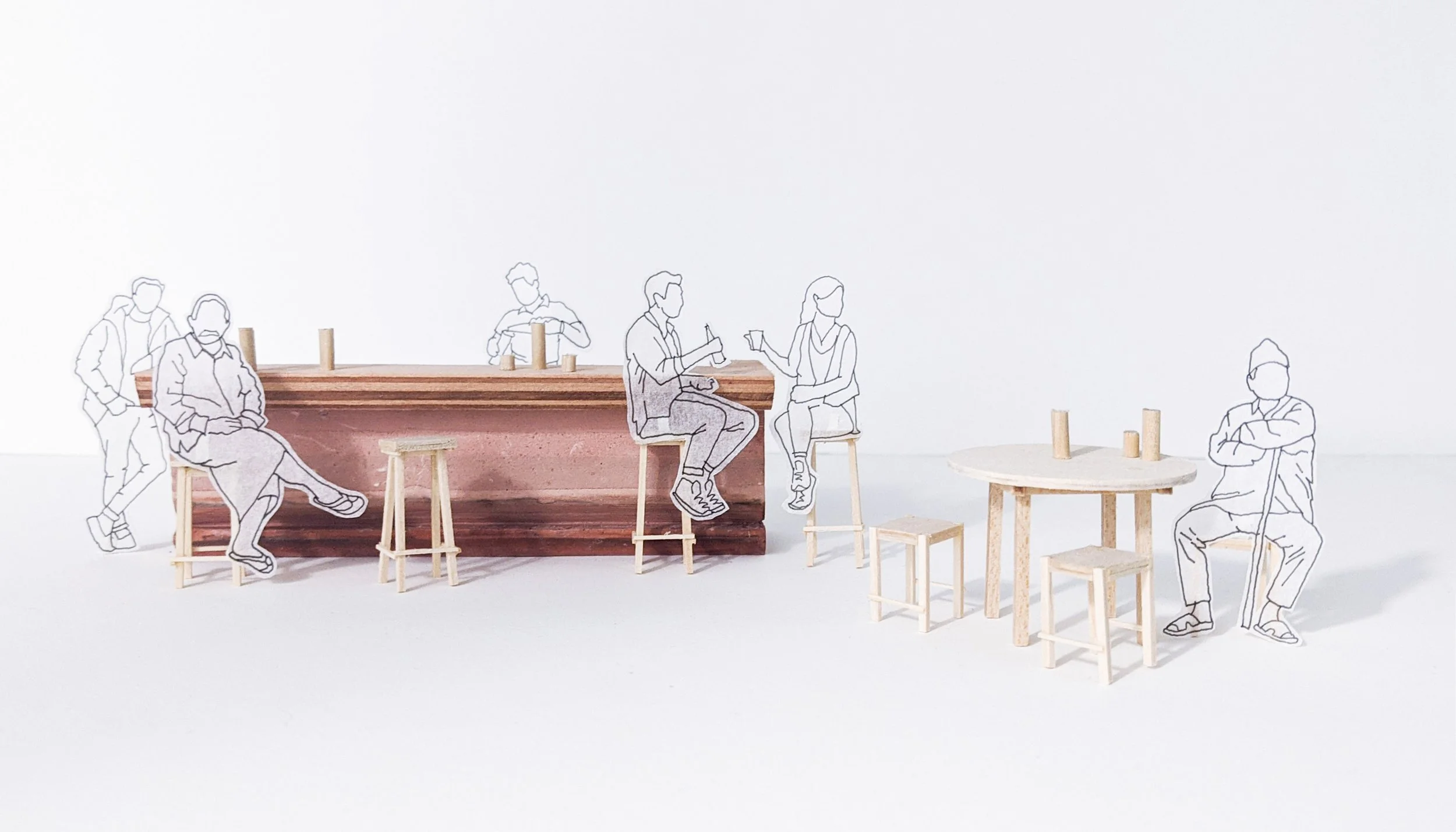 Miniature scene with wooden furniture and paper cutout figures of people, some sitting and some standing, against a plain white background.