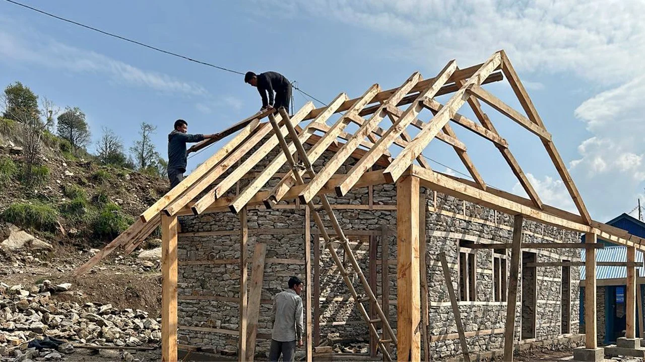 Villagers work on framing the roof of the Ekuwa Health Post in timber, above the heavy stone walls below.