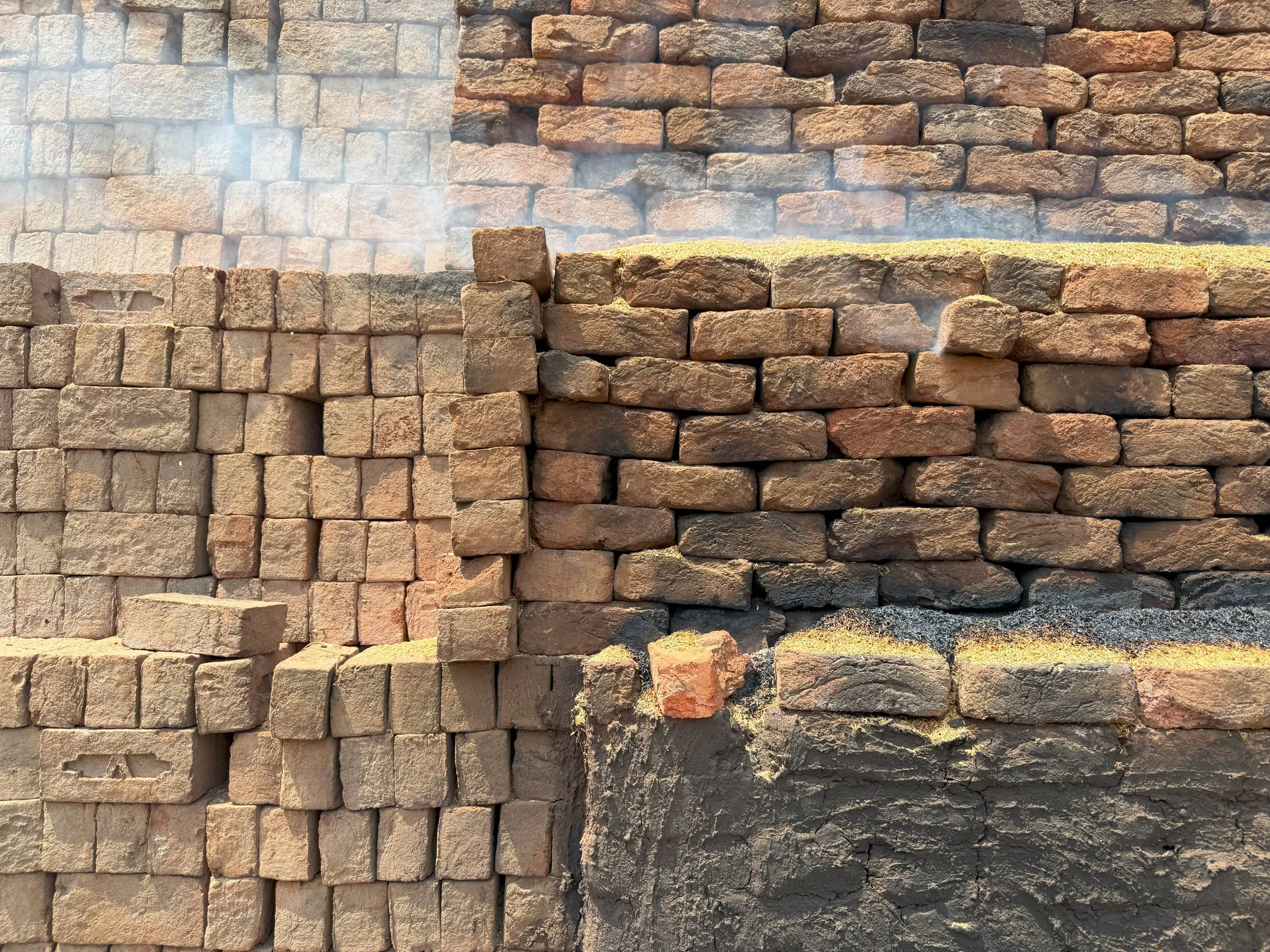 Stacked bricks in beige and reddish tones against a wall with some smoke or mist.