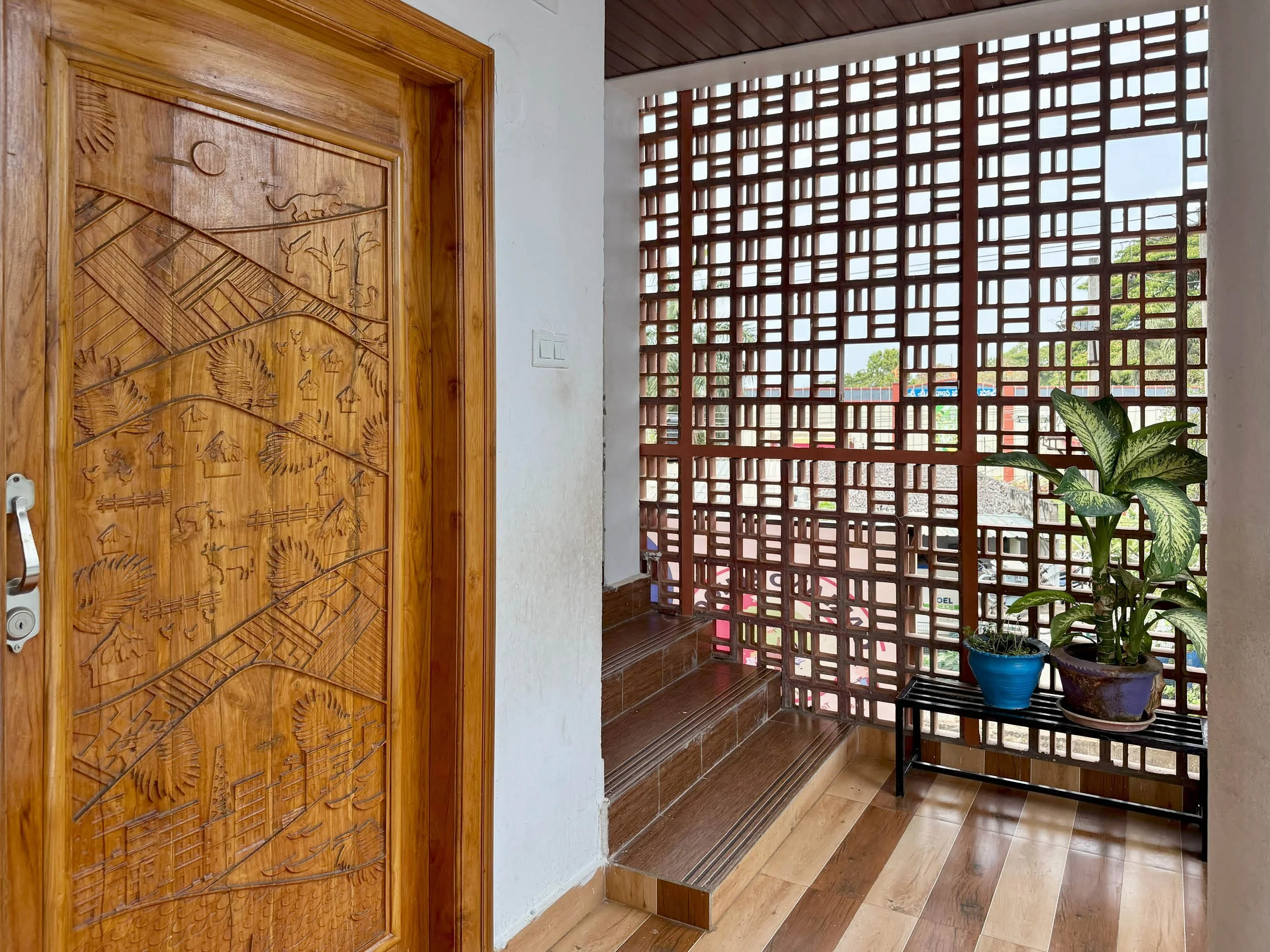 Indoor porch area with wooden steps, a decorative wooden door, large window with wooden lattice, and potted plants.