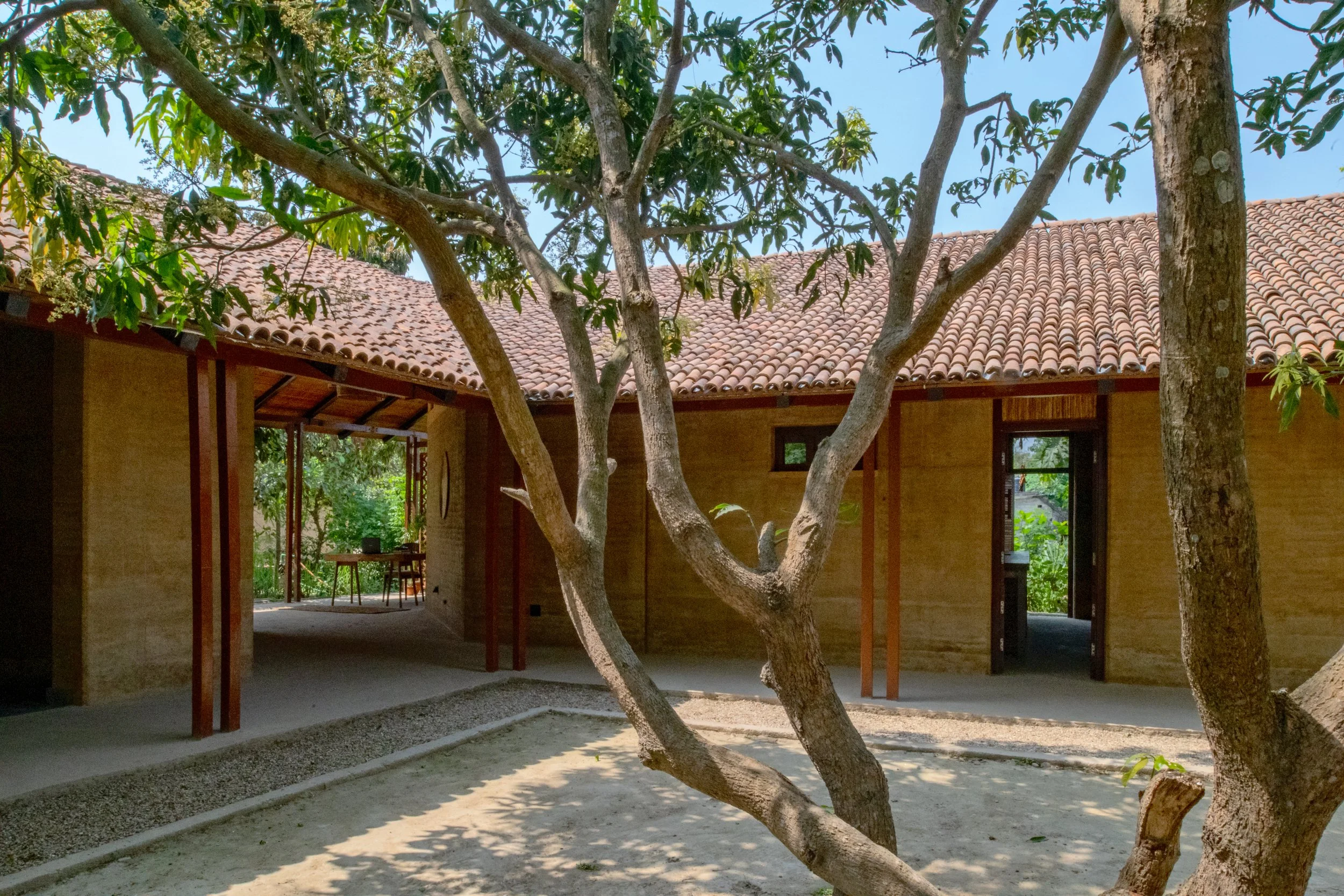A house with a red tile roof seen through trees, with an outdoor patio area and furniture visible.