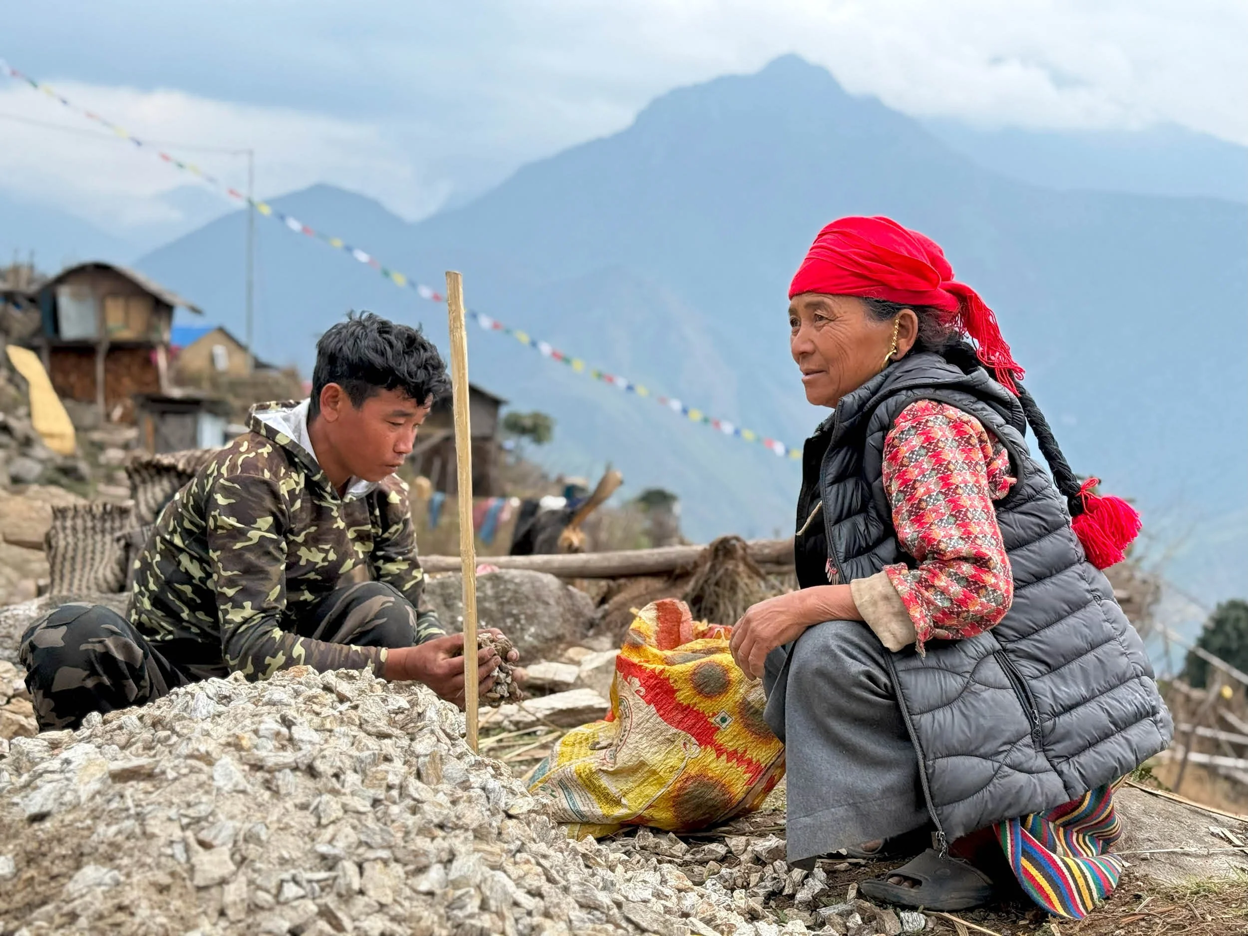 A village woman from Nepal wearing a red headscarf and earrings collects gravel for the construction of the Ekuwa Health Post.