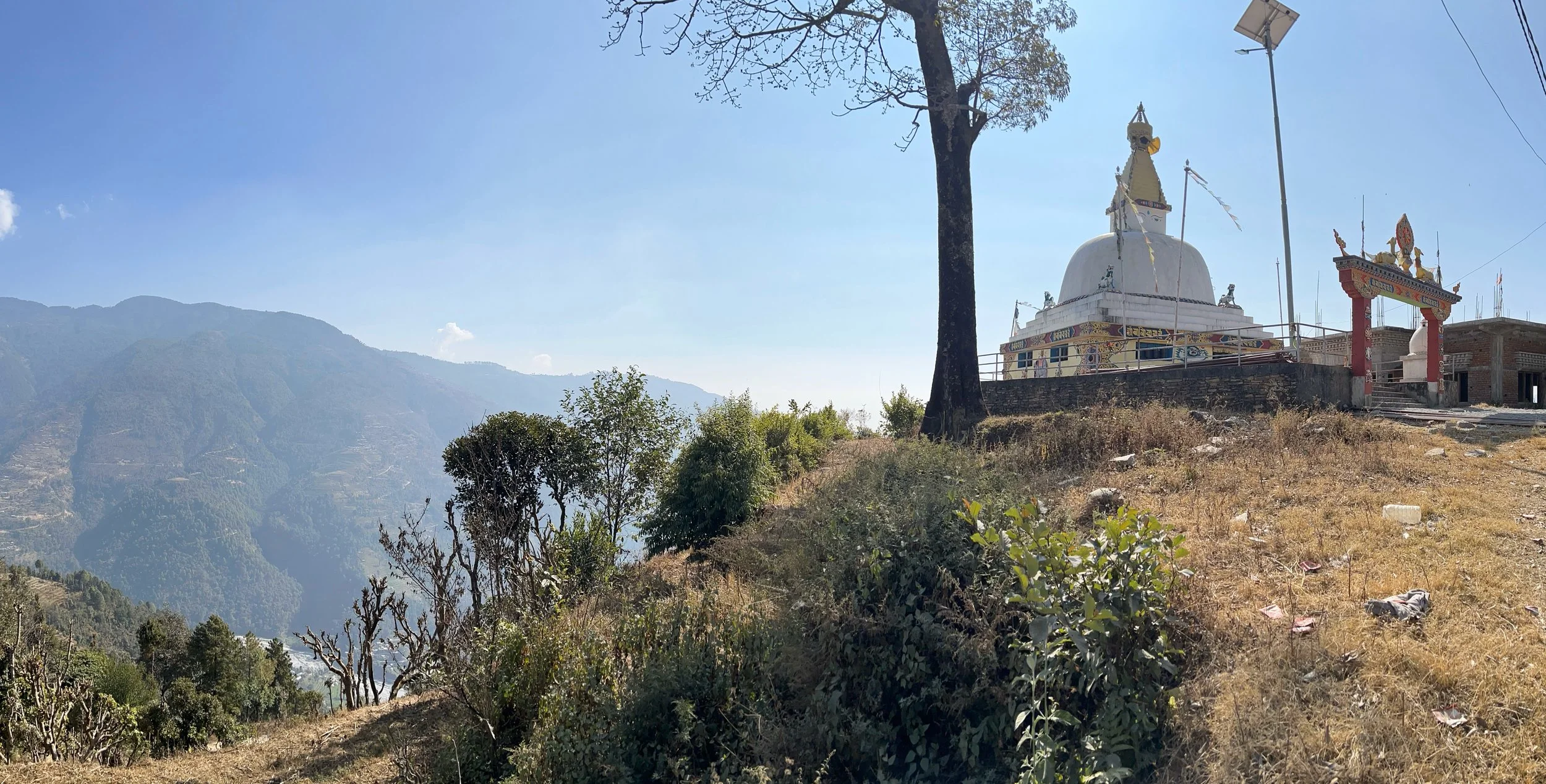 A white Buddhist stupa with colorful decorations on top, situated on a hillside terraced in Ichok, Nepal.