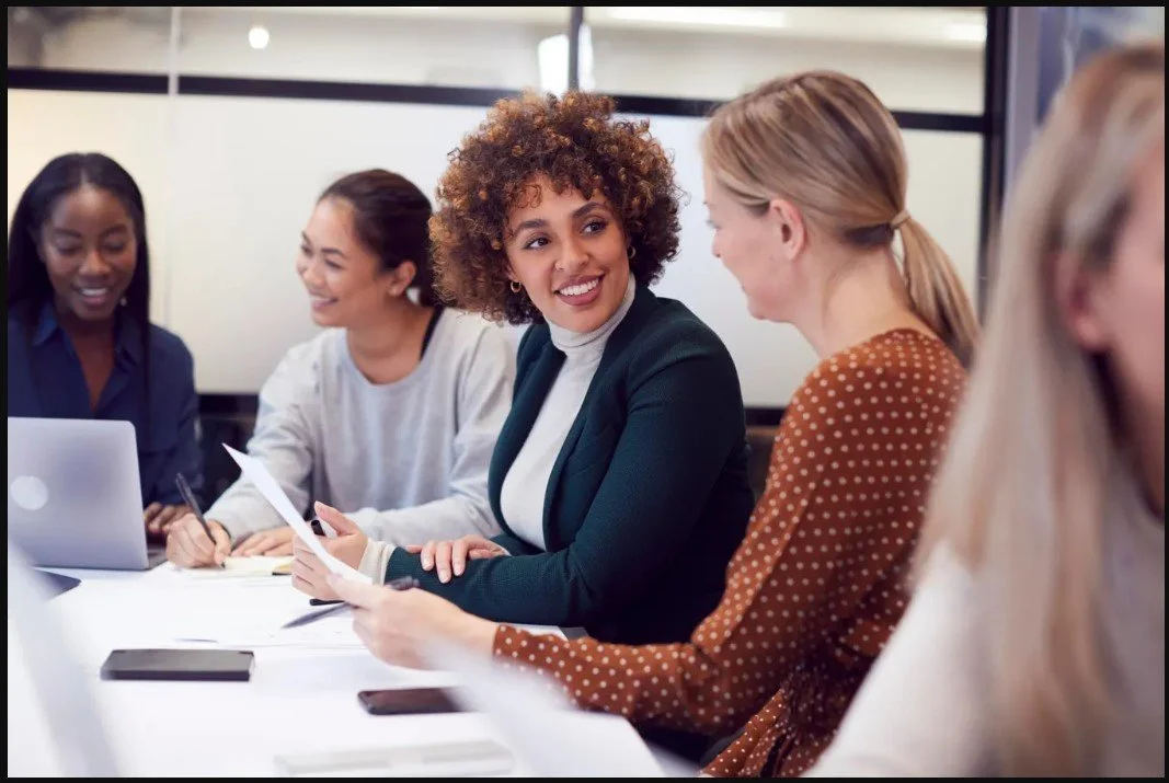 Group of diverse women having a meeting in an office, smiling and engaging in conversation.