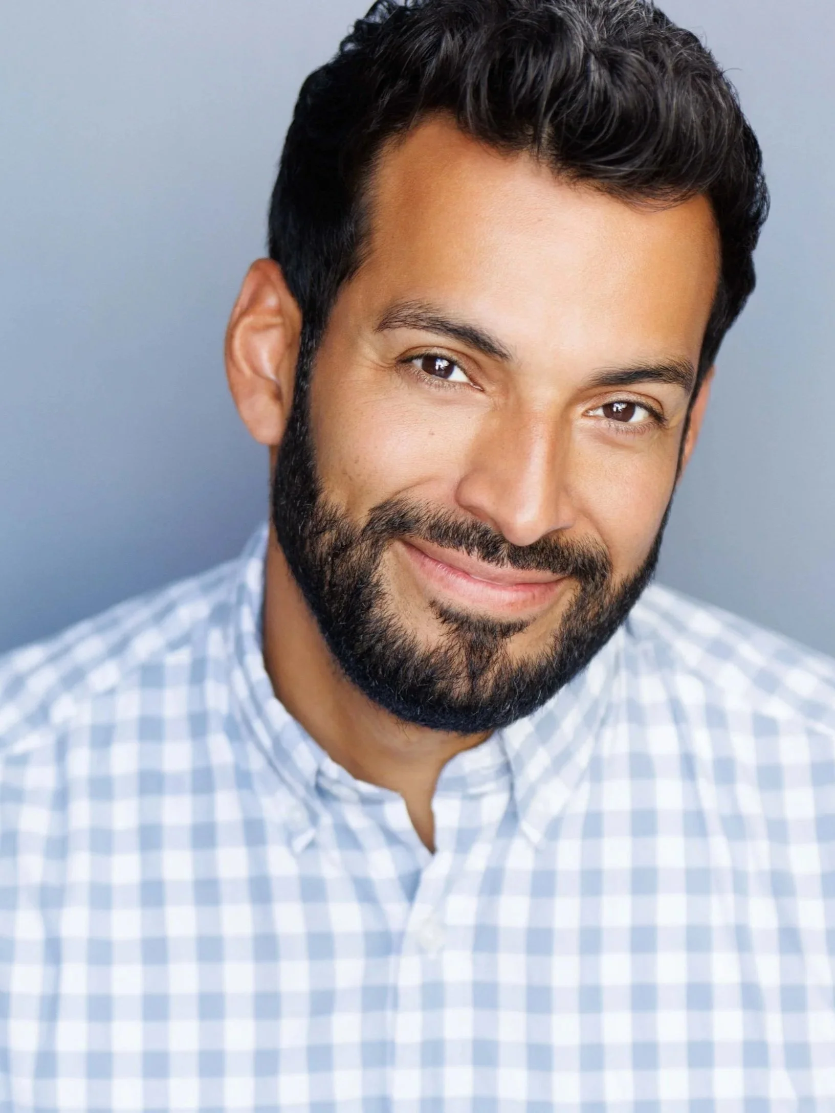 Man smiling in white checkered shirt with blue background actor headshot by tammy brice in minneapolis
