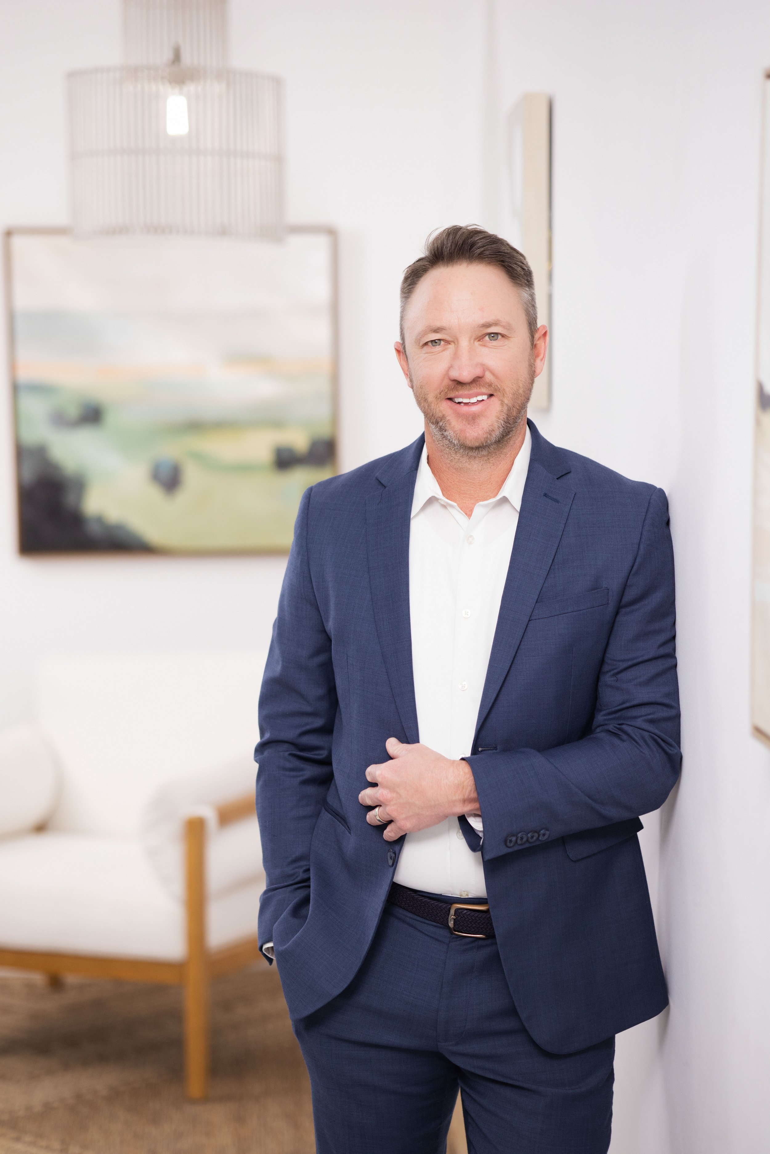 Man in blue suit leaning against a wall and smiling, lifestyle headshot by tammy brice in minneapolis